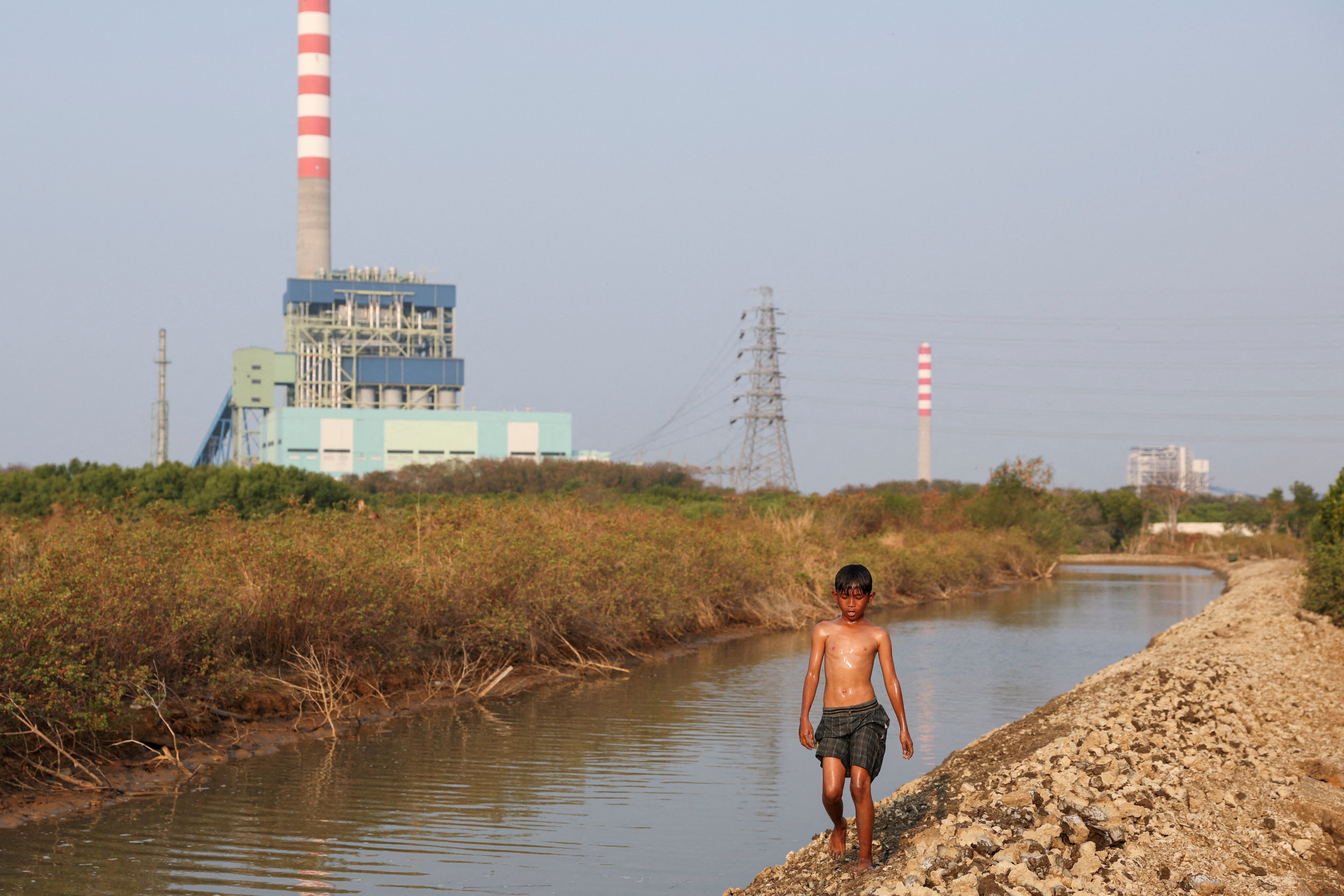 A boy walks beside a canal with the Cirebon-1 coal-fired power plant in the background, in Cirebon, West Java province, Indonesia. Photo: Reuters