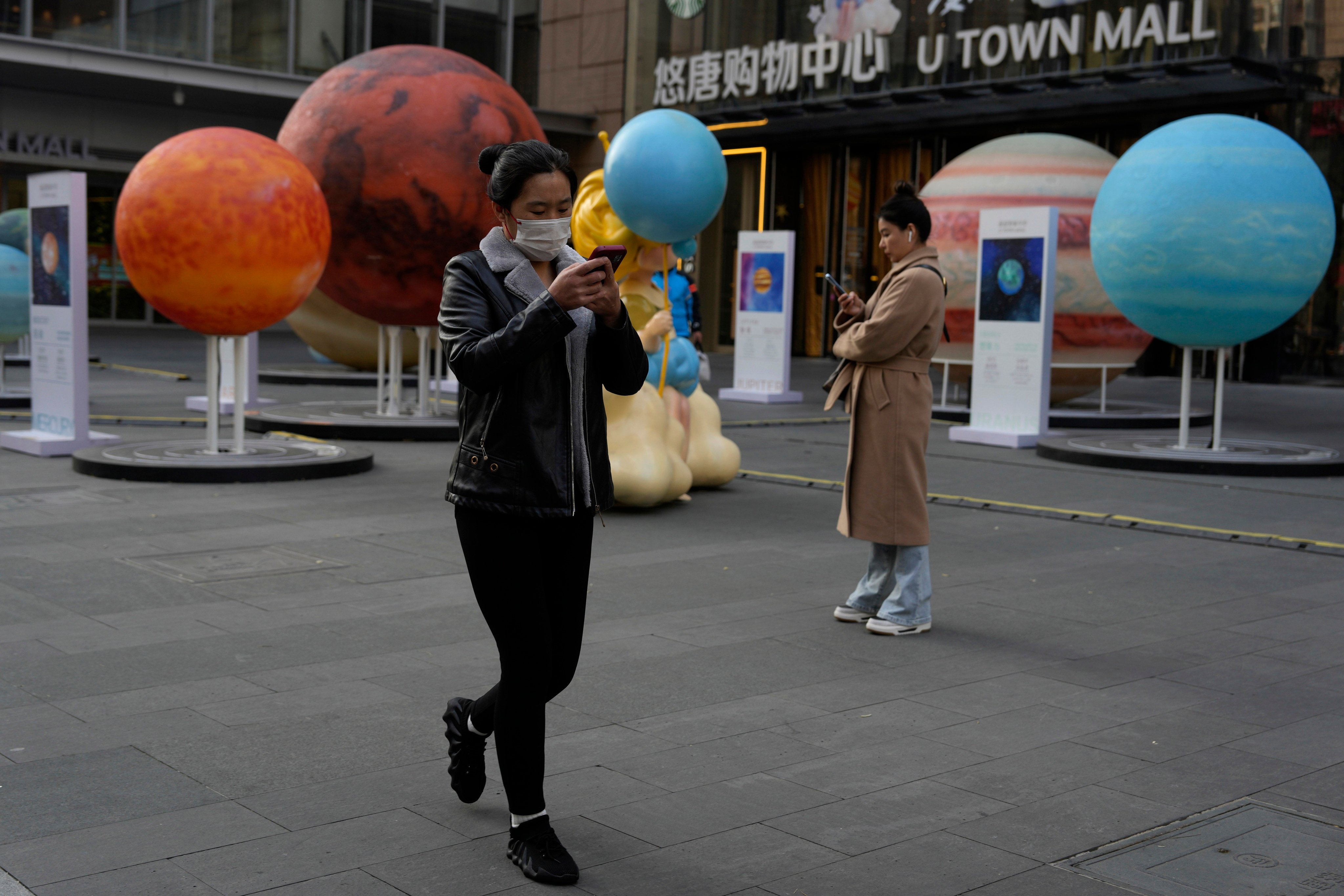 Women look at their phones near a display of planets from the solar system in Beijing on November 19. Photo: AP