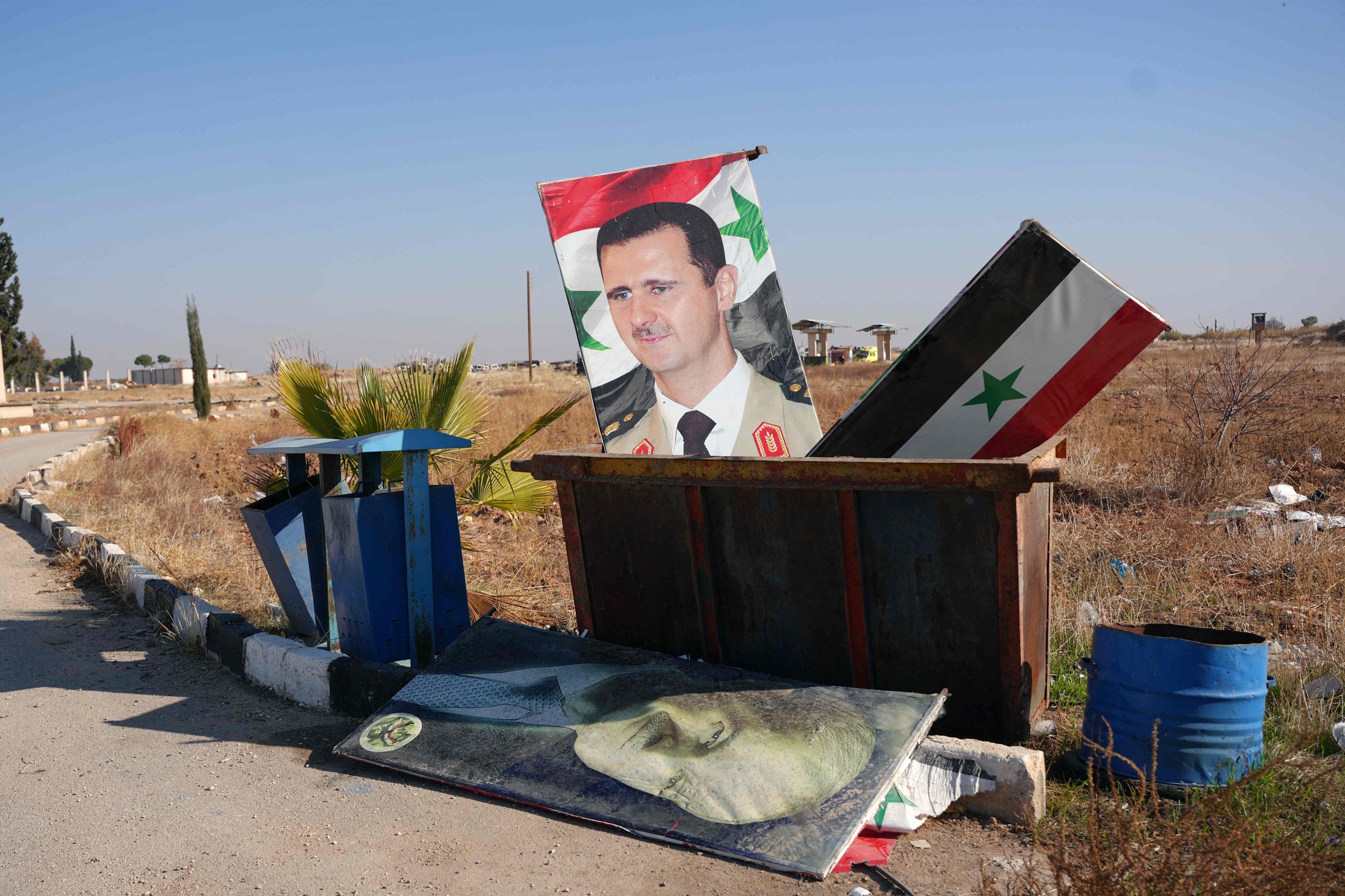 A portrait of Syria’s President Bashar al-Assad and a national flag are seen in a dumpster following the take-over of the Kweyris military airfield by rebel groups. Photo: AFP