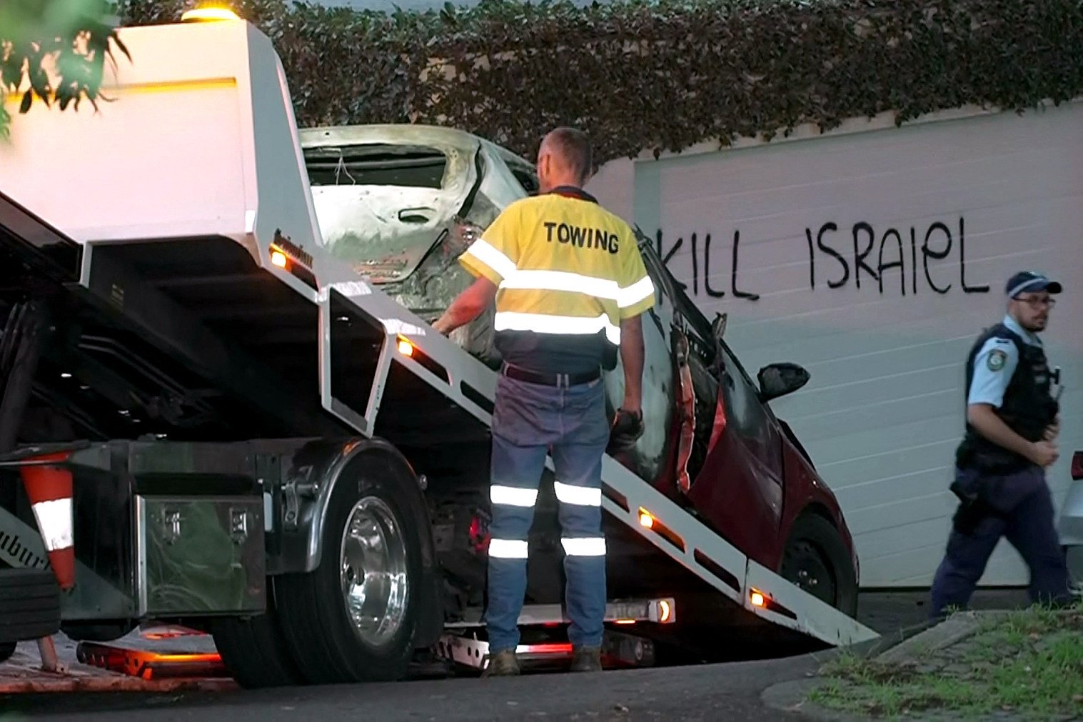 A torched car is removed in the Sydney suburb of Woollahra on Wednesday in front of anti-Israel graffiti written on a wall. Photo: Australian Broadcasting Corporation/AFP