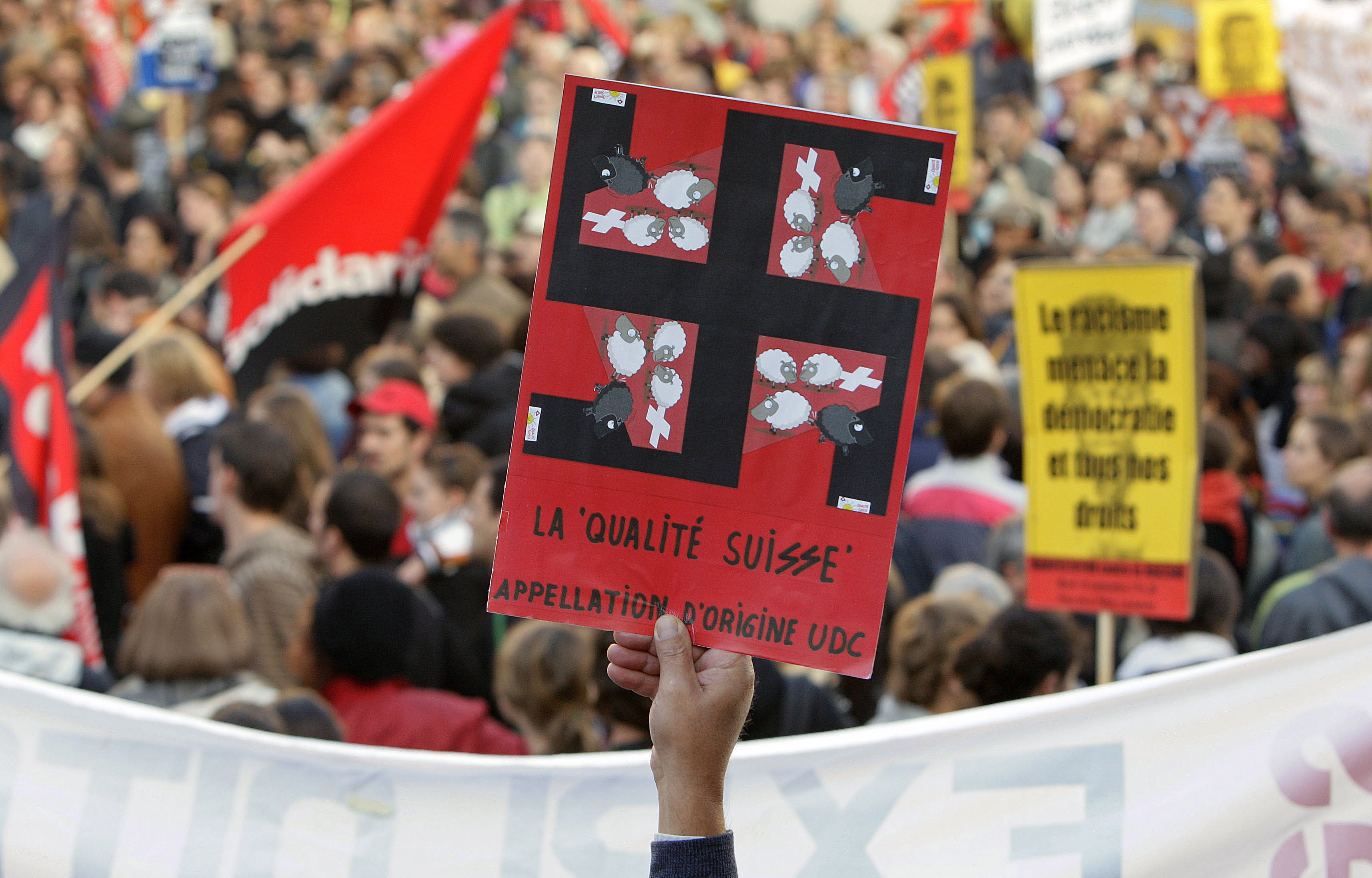 A protester at a rally against the right-wing Swiss People’s Party in September 2007 holds a card with a swastika superimposed on the party’s election poster showing a black sheep being kicked out of the country by three grinning white sheep. Photo: AFP