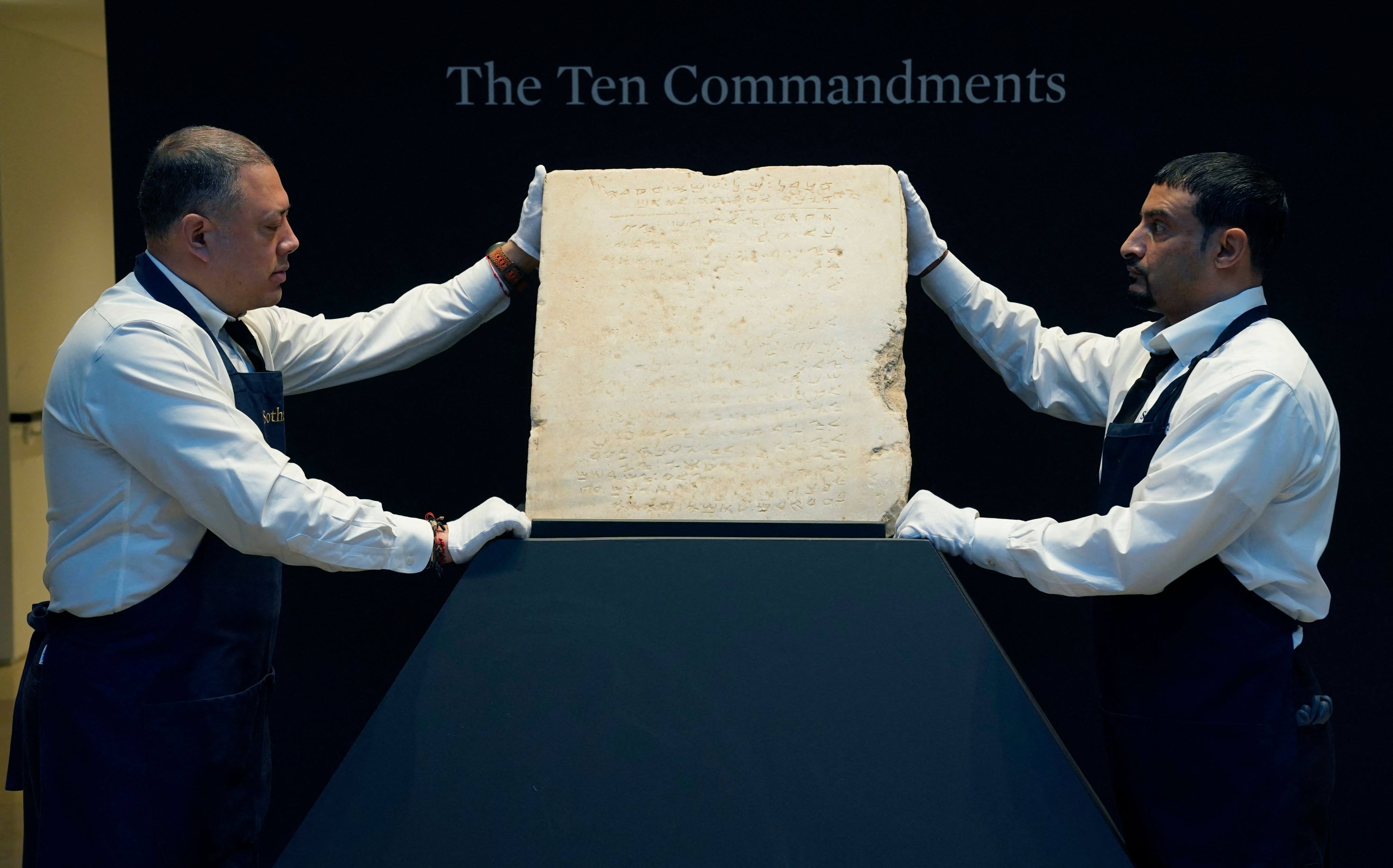 Sotheby’s workers hold what is said to be the oldest known inscribed stone tablet of the Ten Commandments during a press preview in New York on December 9. Photo: AFP