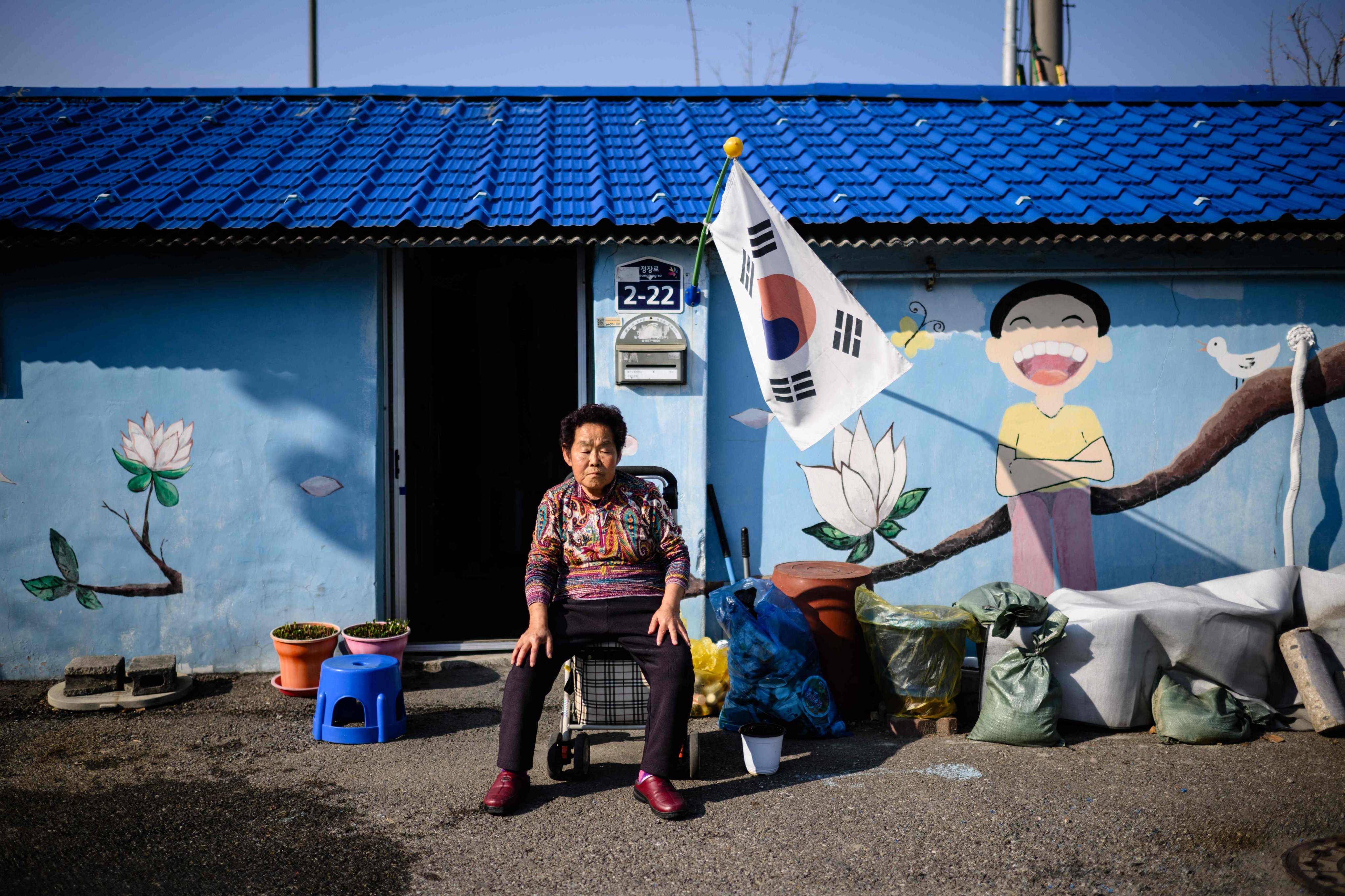 An elderly woman rests her eyes while sitting in front of a mural outside a property in Dongducheon, Gyeonggi Province. Photo: AP