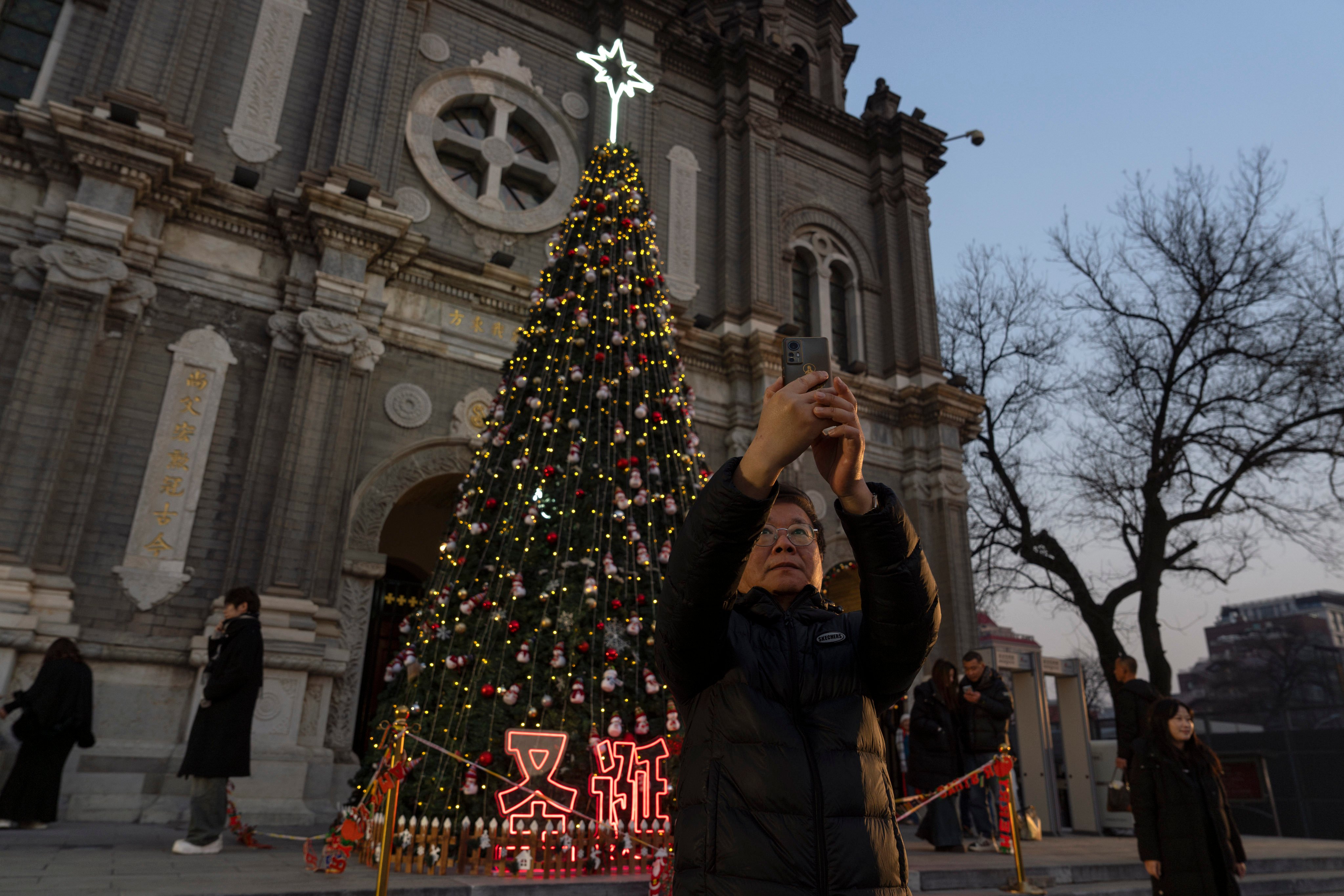 A visitor takes a selfie with a Christmas tree on the eve of Christmas outside a church in Beijing on December 24, 2024. Photo: AP