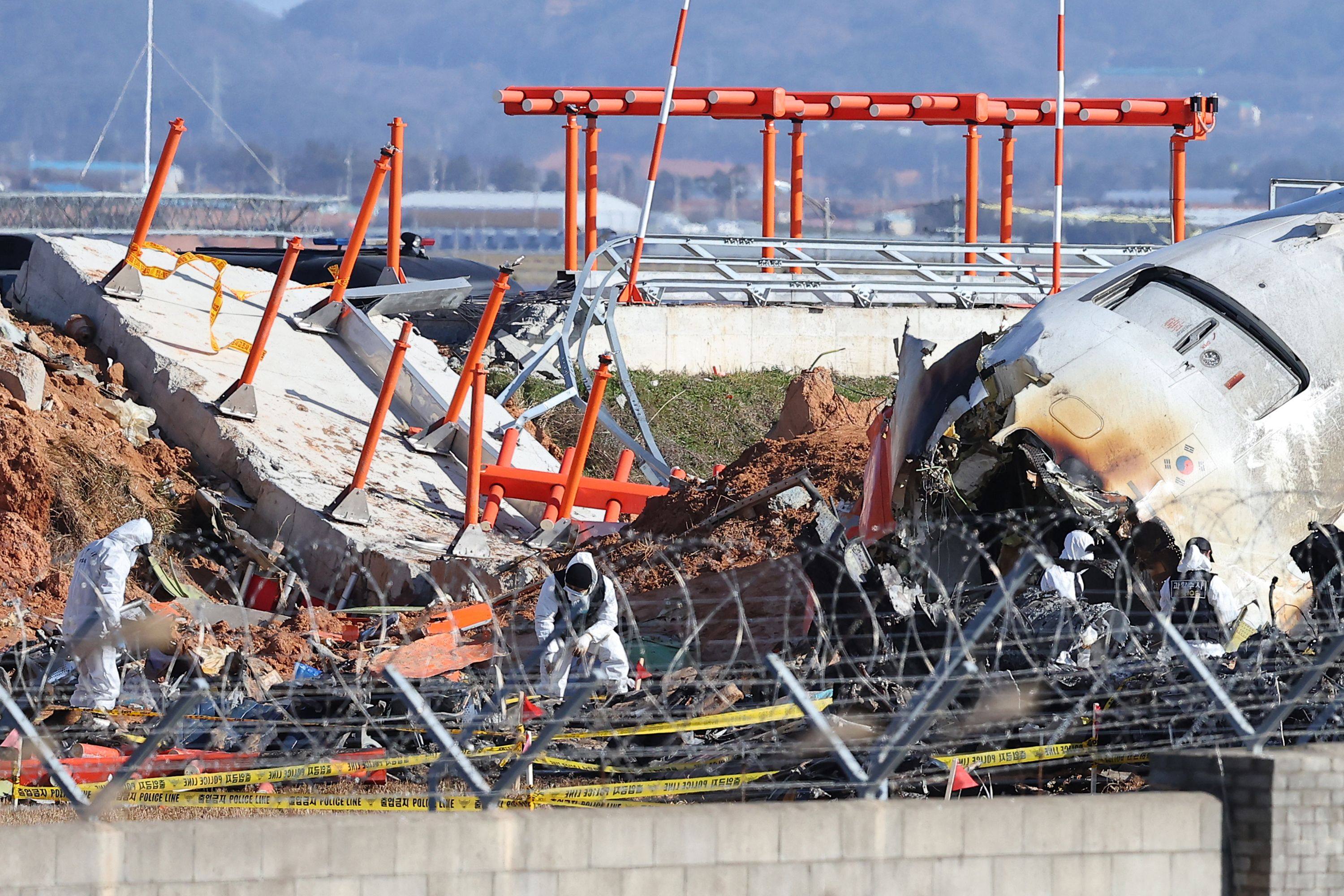 Police forensics personnel and National Bureau of Investigation officials are seen by a wall as they work at the scene of the Jeju Air plane crash at Muan International Airport in South Korea on December 31. Photo: Yonhap / AFP