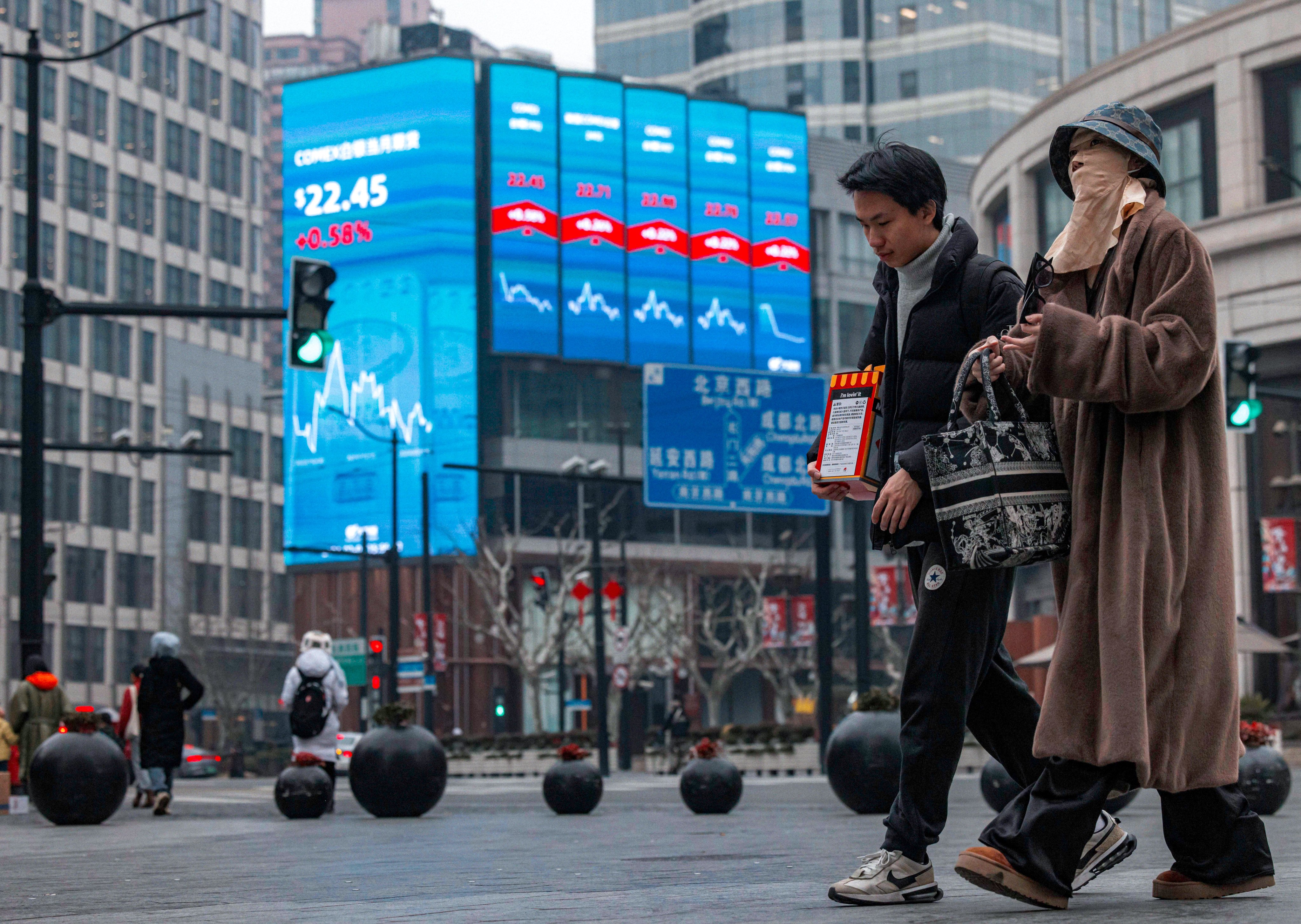 People walk on the street near a large screen showing stock and index levels in Shanghai in February 2024. Photo: EPA-EFE