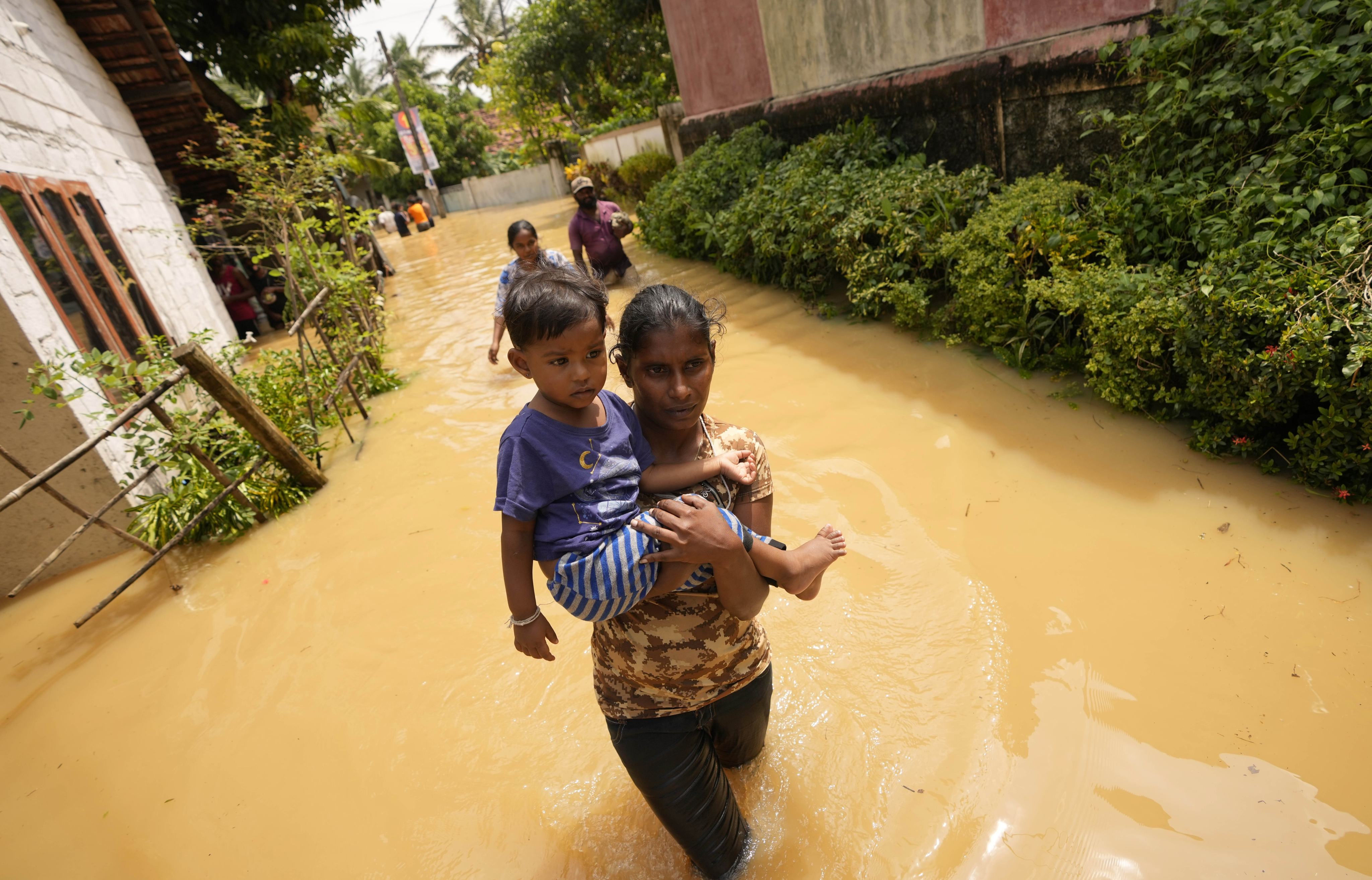 A Sri Lankan woman carries a child as she wades through a flooded street north of Colombo, Sri Lanka, in 2021. Photo: AP