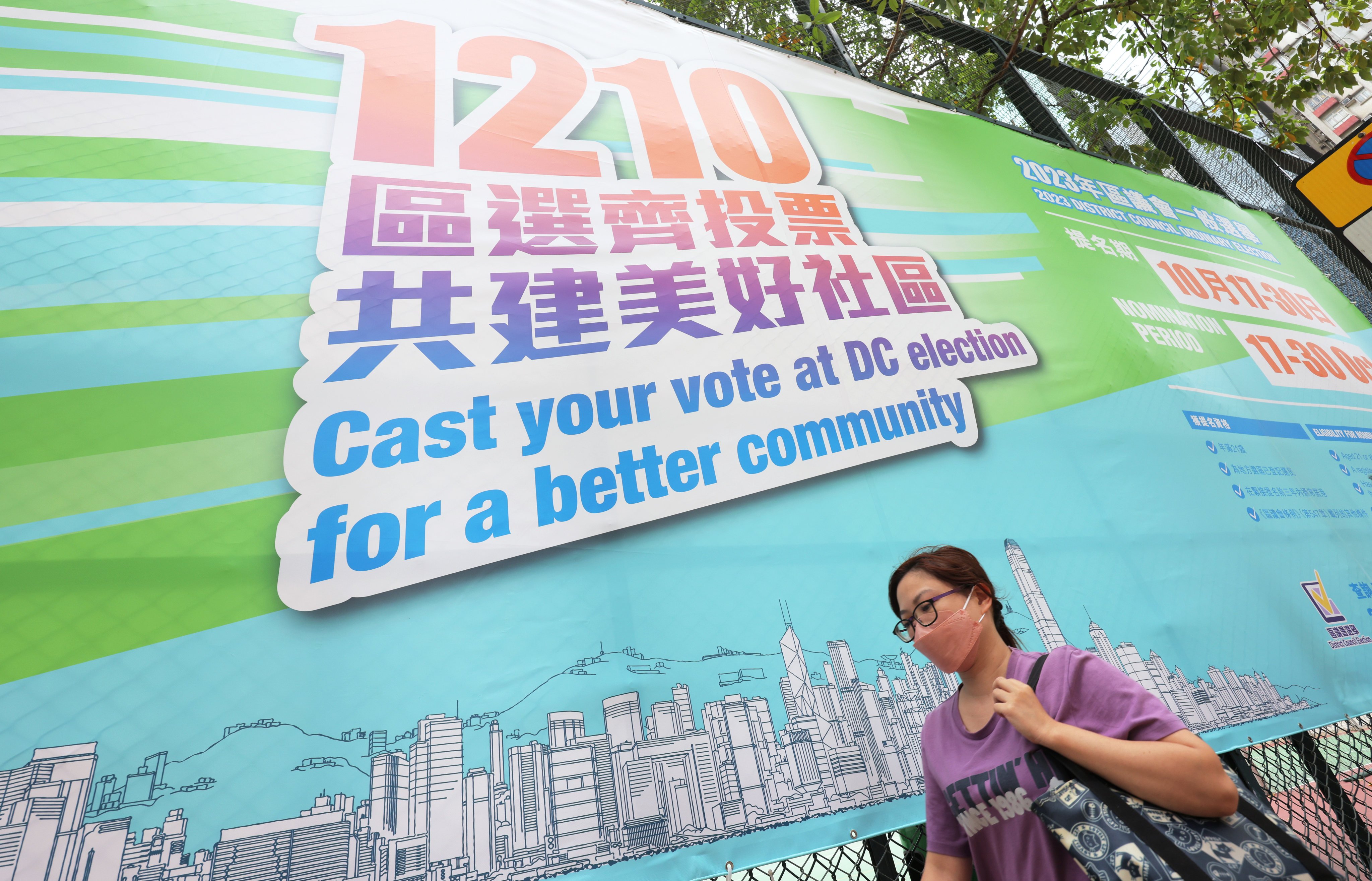 A woman walks past a promotional poster for the 2023 district council elections. Photo: Jelly Tse