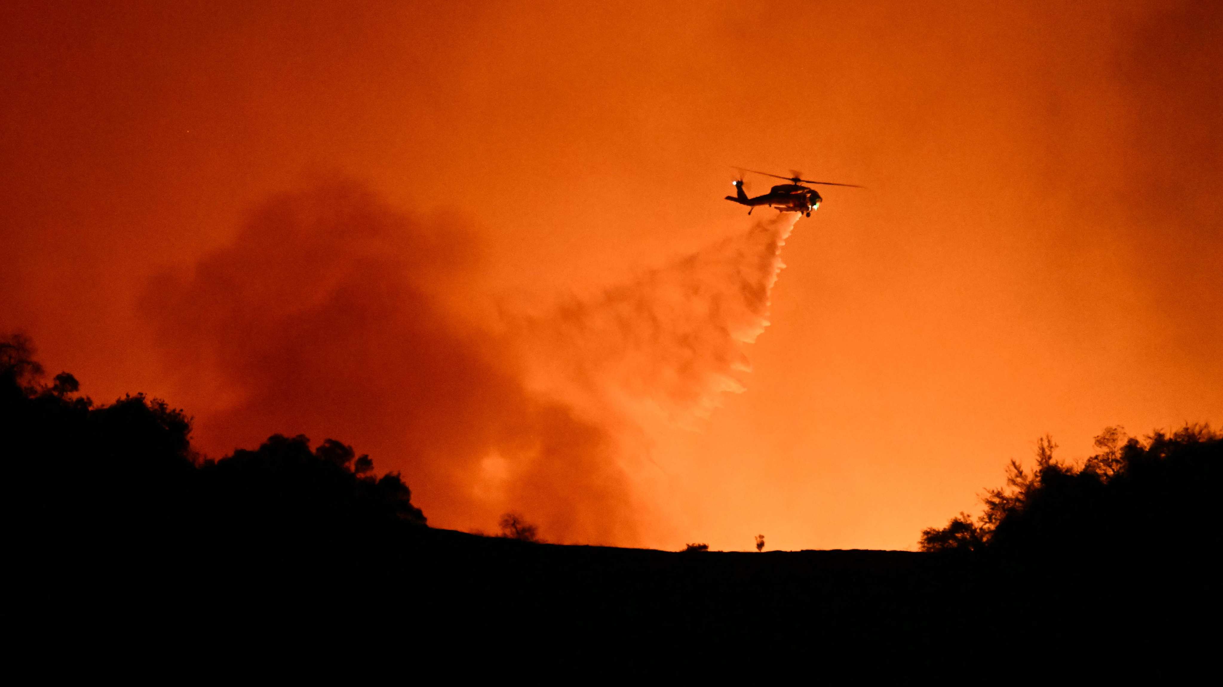 A helicopter drops water on smoke and flames from the Palisades fire burning in Los Angeles. Photo: AFP