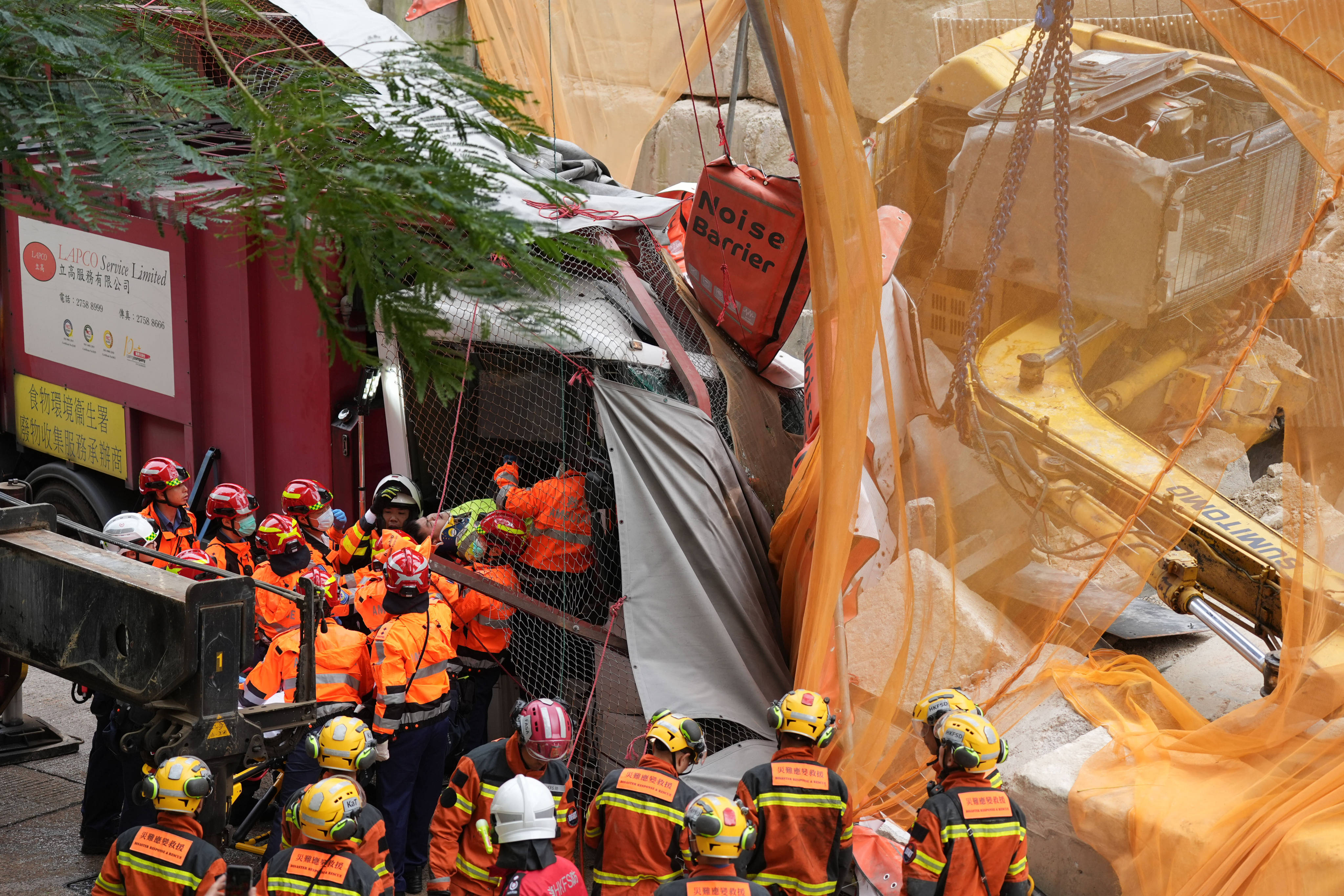 An excavator rolled down a slope and crashed into a sound barrier and a garbage truck in Lam Tin, injuring three workers. Photo: Eugene Lee