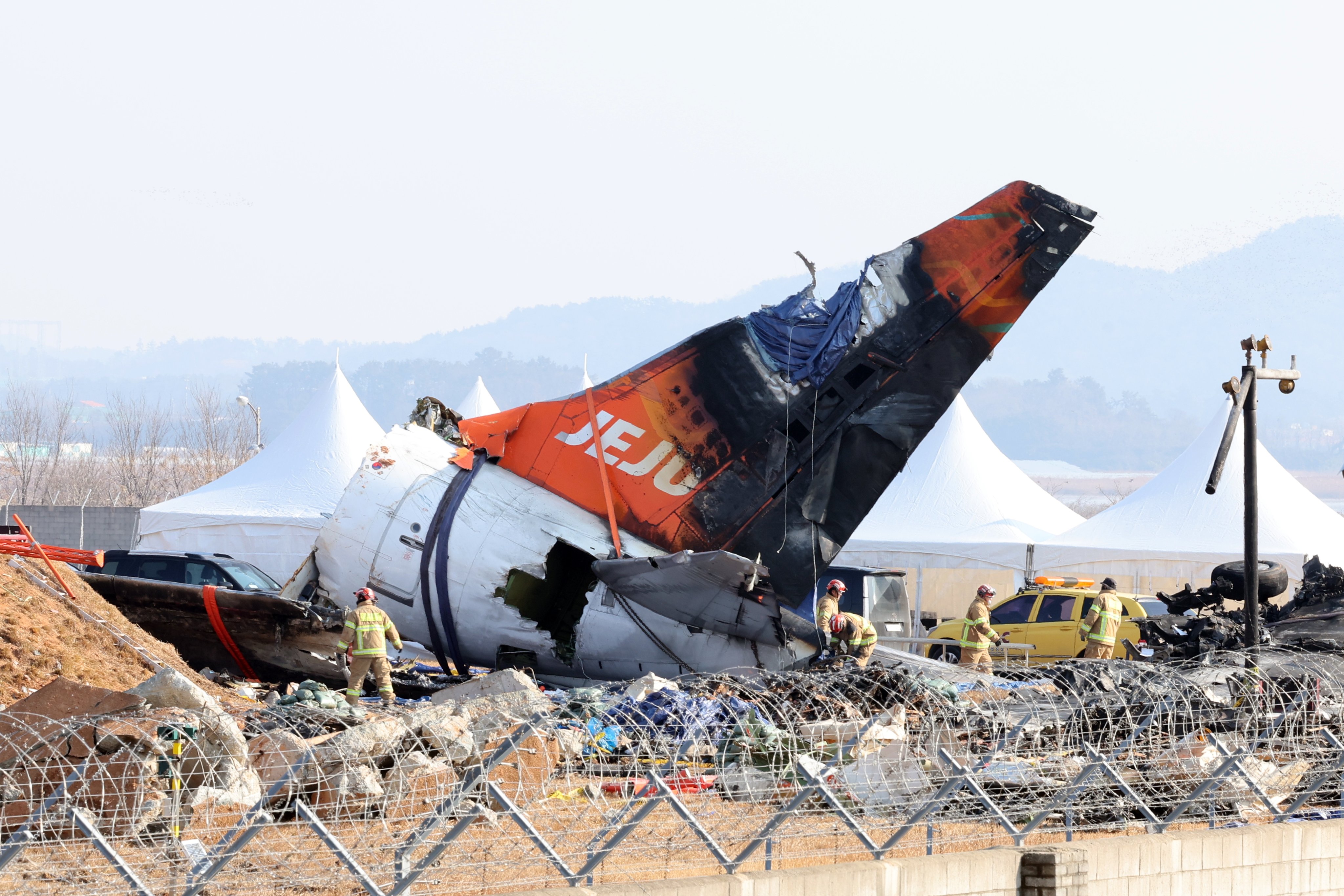 Firefighters remove tarpaulin sheets covering the debris of the crashed Jeju Air jet at Muan airport in South Korea on January 13. Photo: EPA-EFE/Yonhap