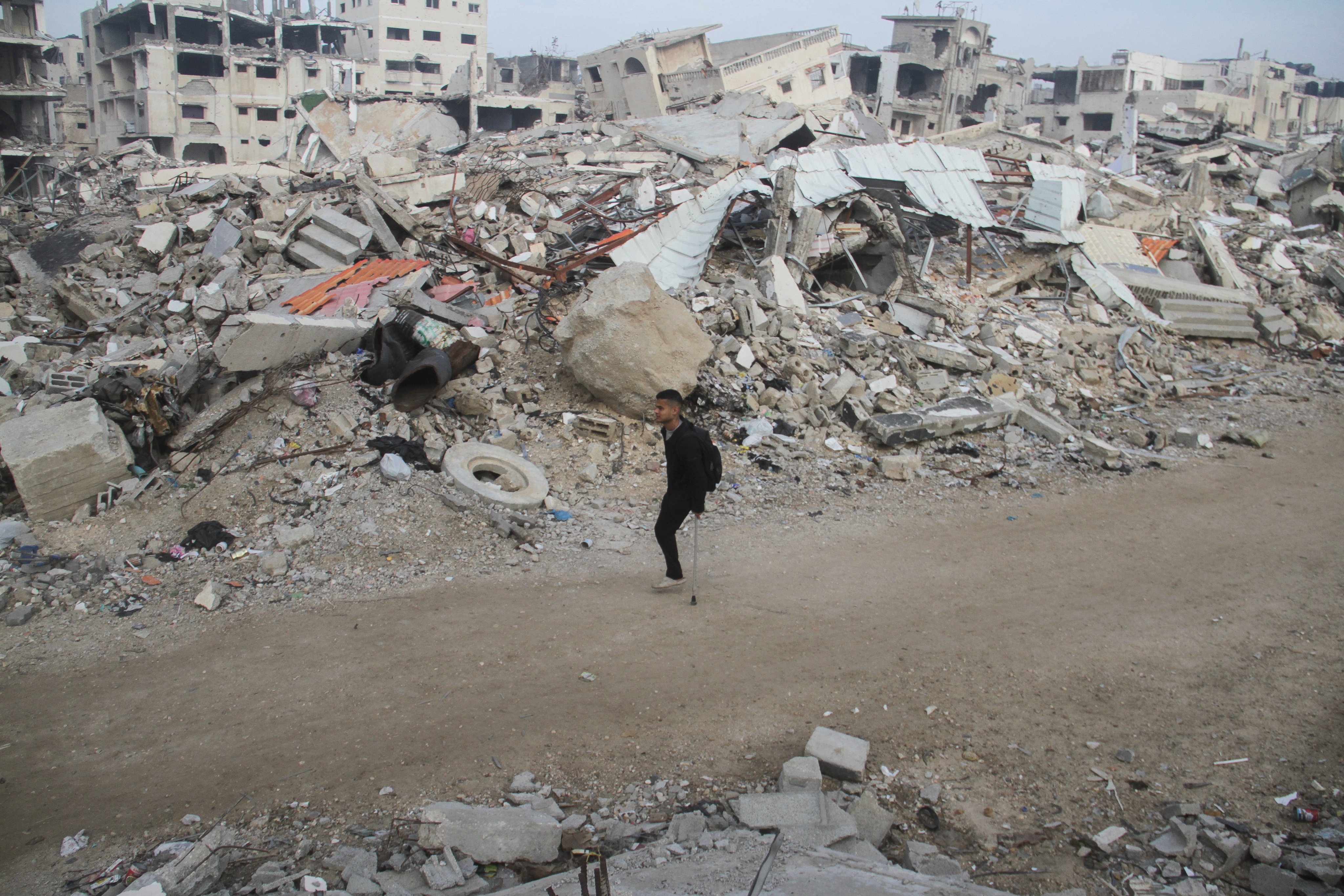 A Palestinian man walks with a crutch past the rubble of buildings destroyed in Israeli strikes. Photo: Reuters