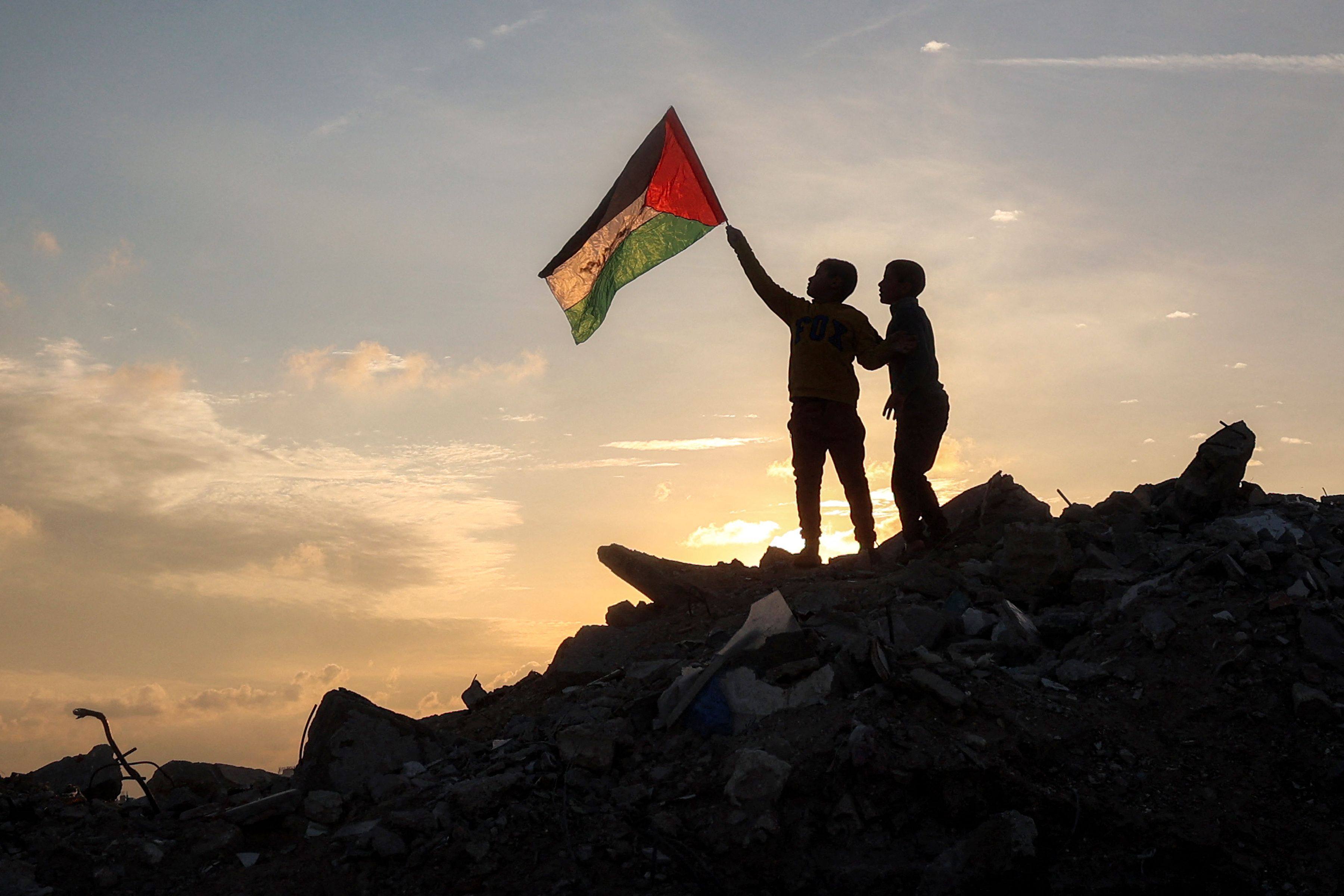 A boy holds a Palestinian flag atop a mound of rubble at a camp for people displaced by conflict in the Gaza Strip on Friday. Photo: AFP