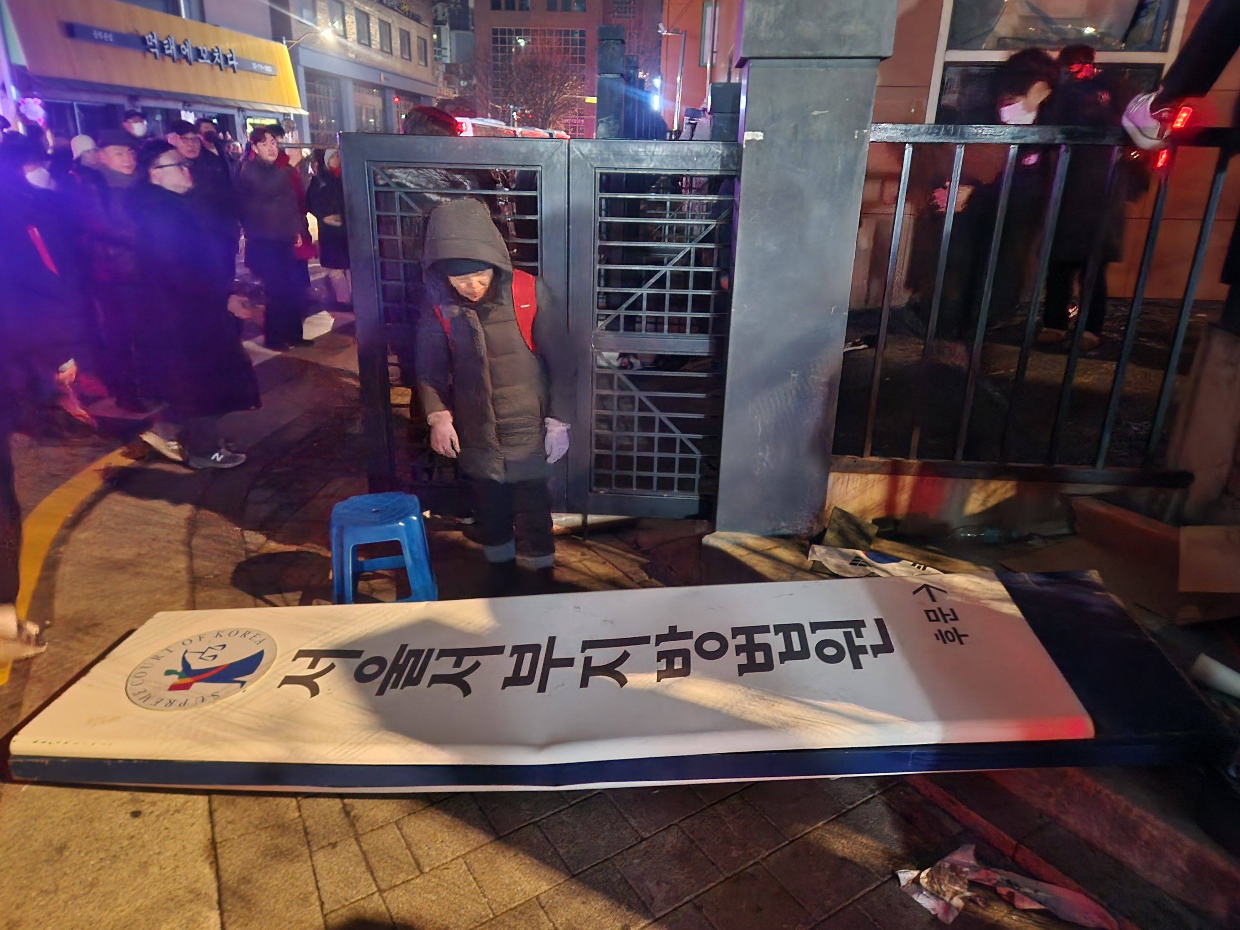 Supporters of impeached South Korean President Yoon Suk-yeol walk past a broken signboard at the Seoul Western District Court on Sunday. Photo: Yonhap via AFP