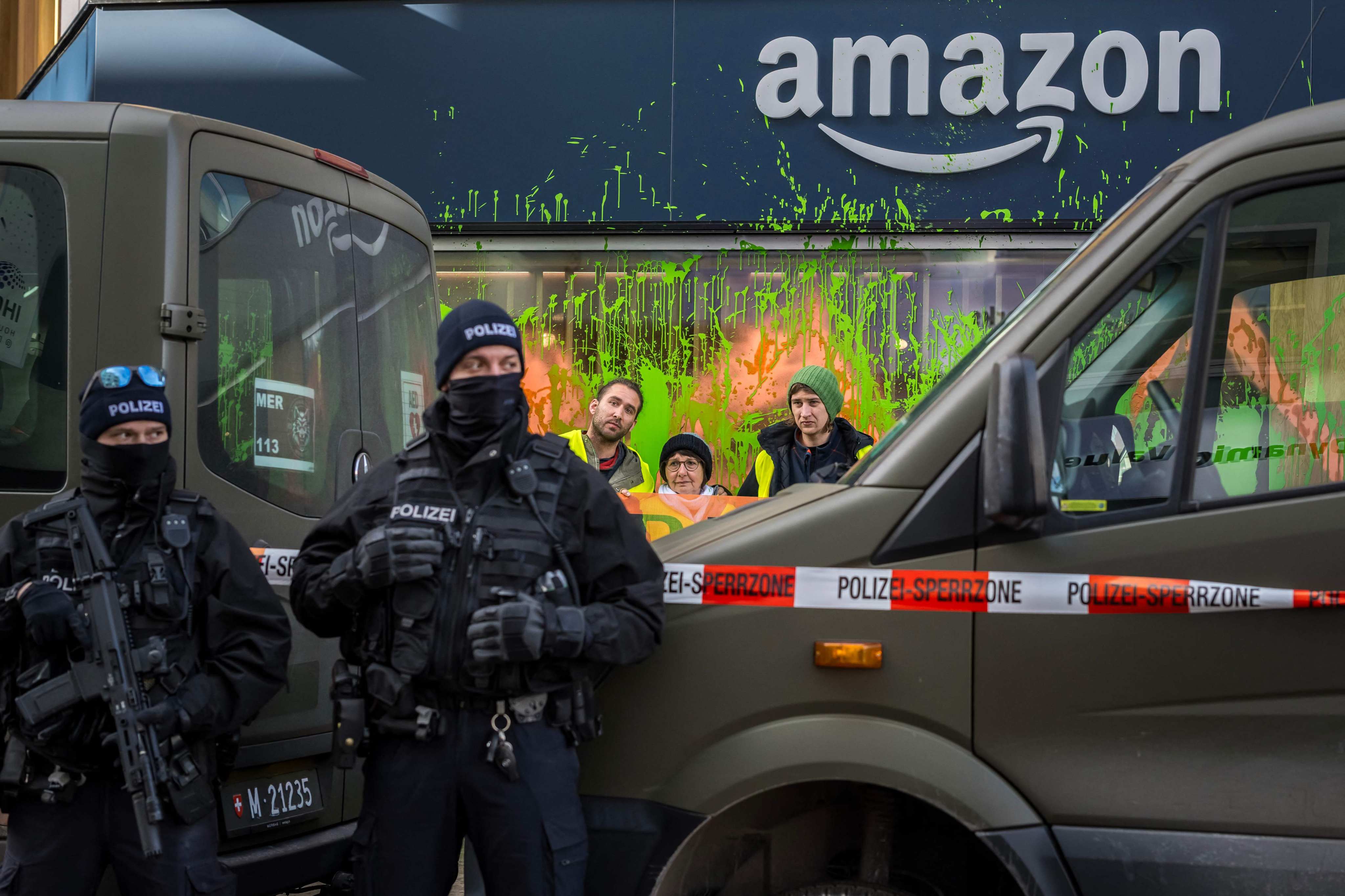 Climate activists hold a banner as they stand behind police after they painted the windows of the Amazon booth during the World Economic Forum (WEF) annual meeting in Davos, Switzerland on Monday. Photo: AFP