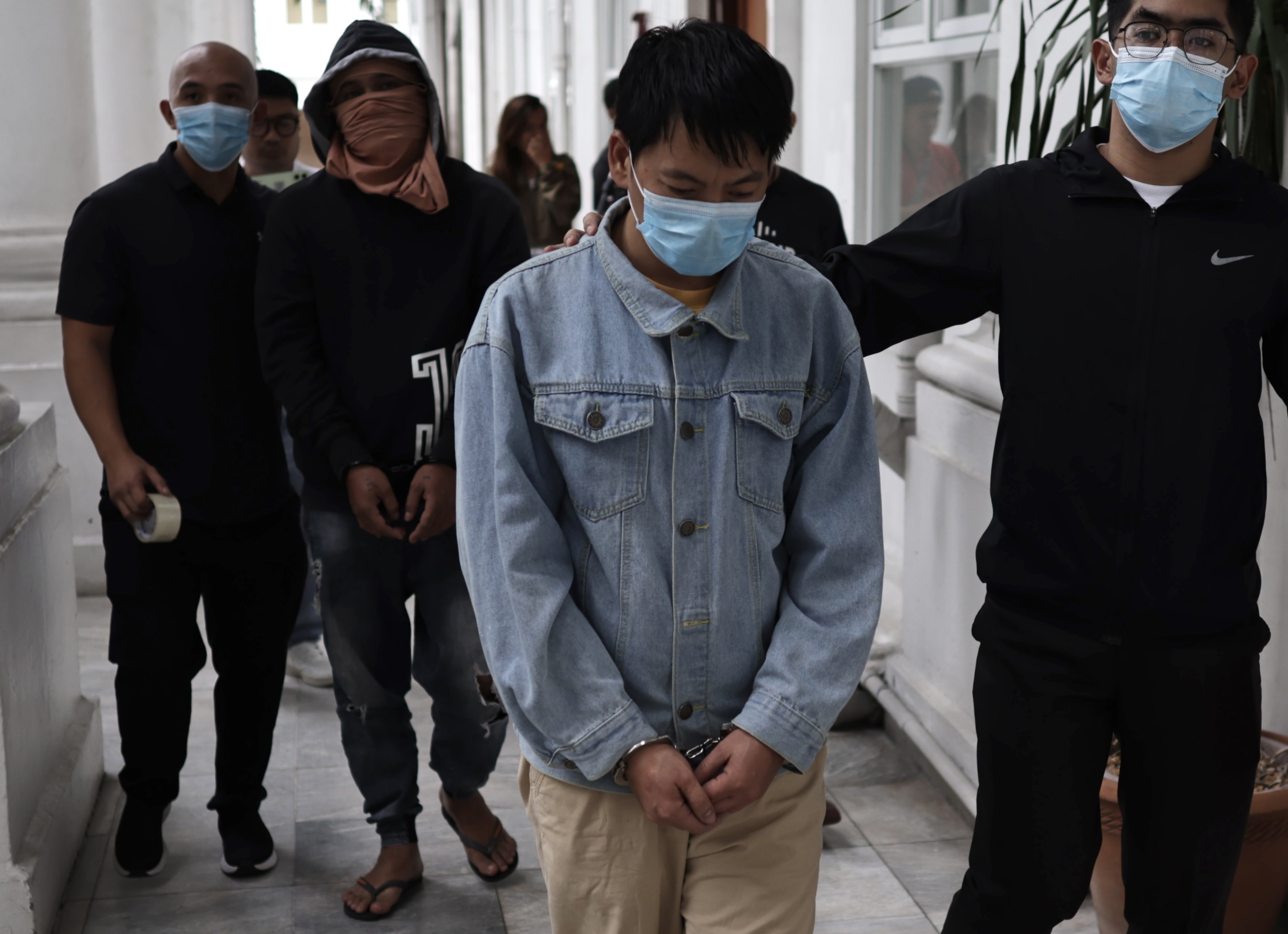 Chinese national Deng Yuanqing (middle) with an unidentified Filipino companion in handcuffs escorted to the Department of Justice office in Manila on Monday. Photo: EPA-EFE