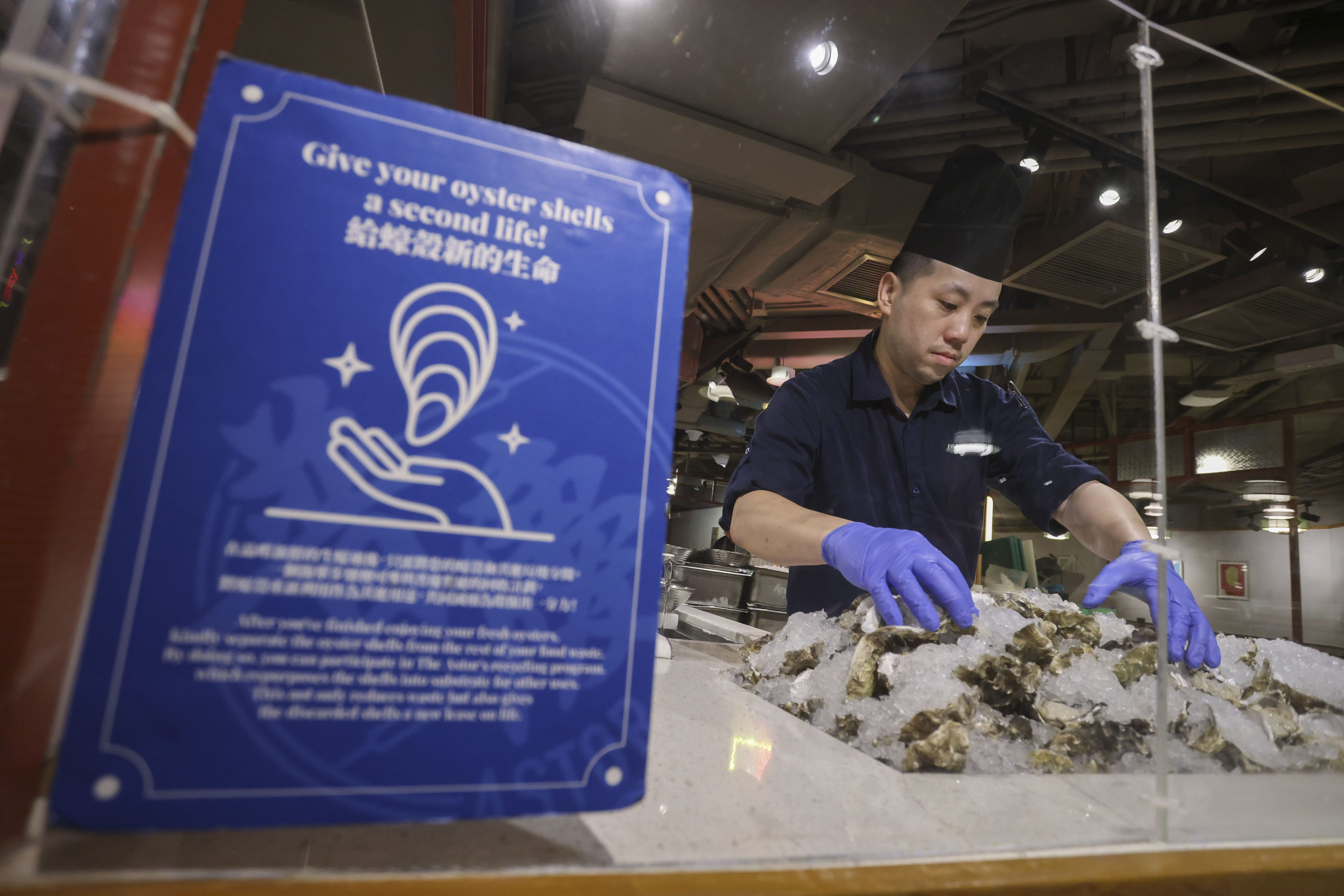 A sign asking “Give your oyster shells a second life!”requesting patrons to separate the oyster shells, at The Astor, at Eaton HK. Hong Kong hotels have teamed up with a local cement manufacturer to replace 80 per cent of limestone needed for production with oyster shells, a scheme that hoteliers said was the world’s first attempt the hospitality sector did to decarbonise one of the worst greenhouse gas emitting industries. 16AUG24 SCMP / Jonathan Wong