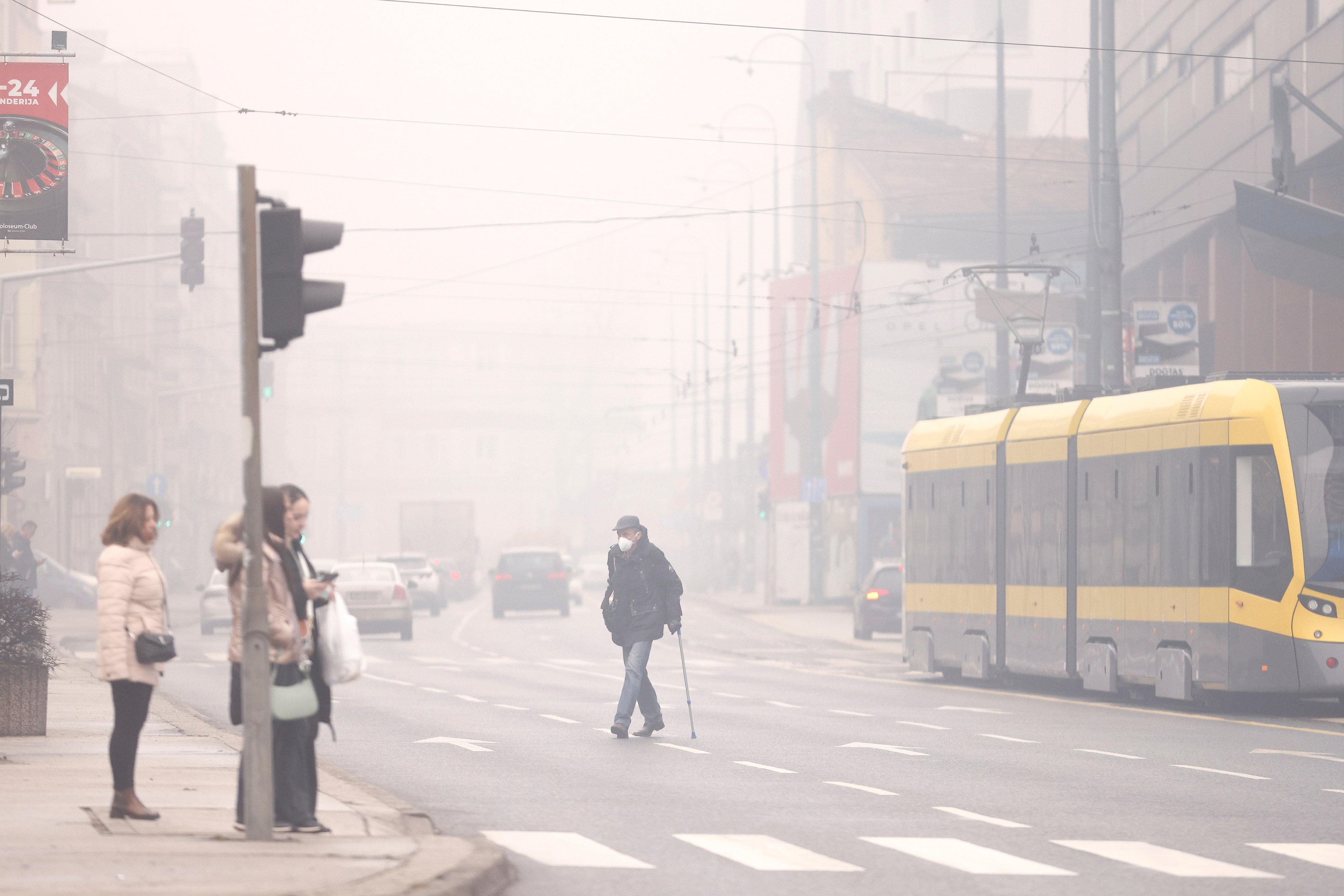 A man wearing a face mask to protect from air pollution crosses the street shrouded by pollution haze as smog covers Sarajevo, Bosnia on Wednesday, January 22, 2025. Photo: AP