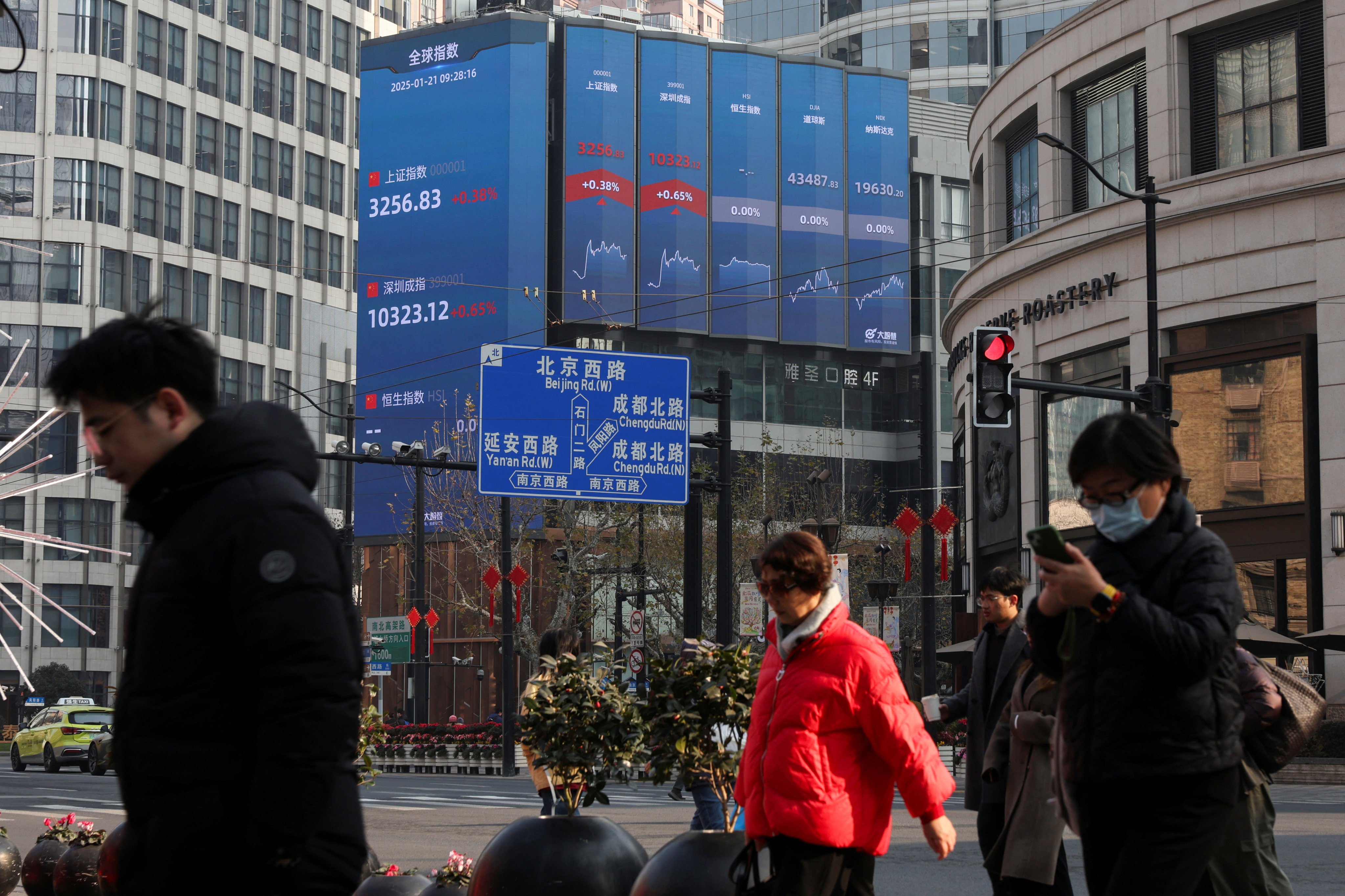 Pedestrians crossing a street in Shanghai as an electronic billboard shows key stock indexes on January 21, 2025. Photo: Reuters