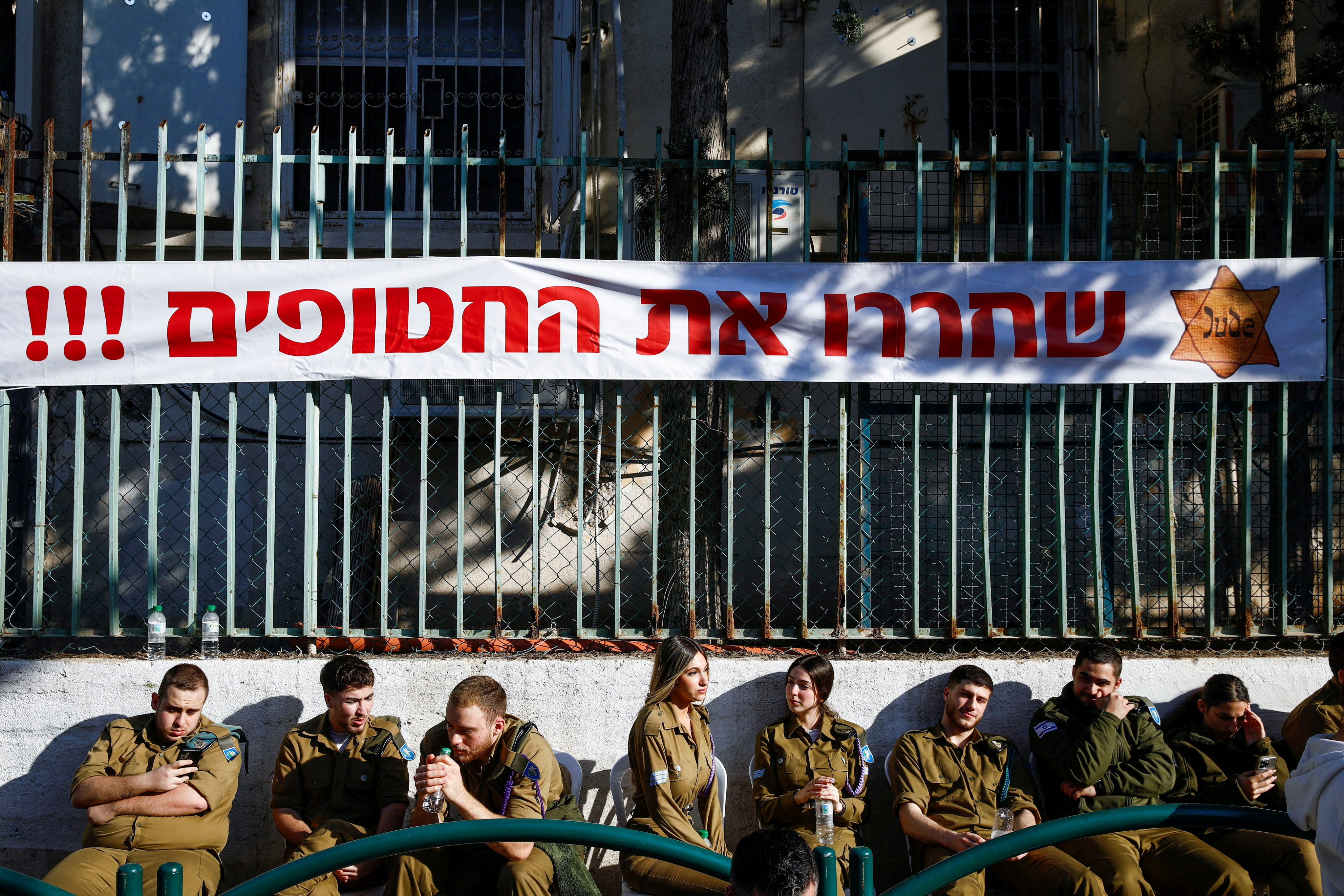 Soldiers sit under a banner, with a yellow Star of David, that reads “Release the hostages!” on the day of the 80th anniversary of the liberation of the Auschwitz-Birkenau Nazi concentration camp, at a ceremony in Haifa, Israel on Monday. Photo: Reuters