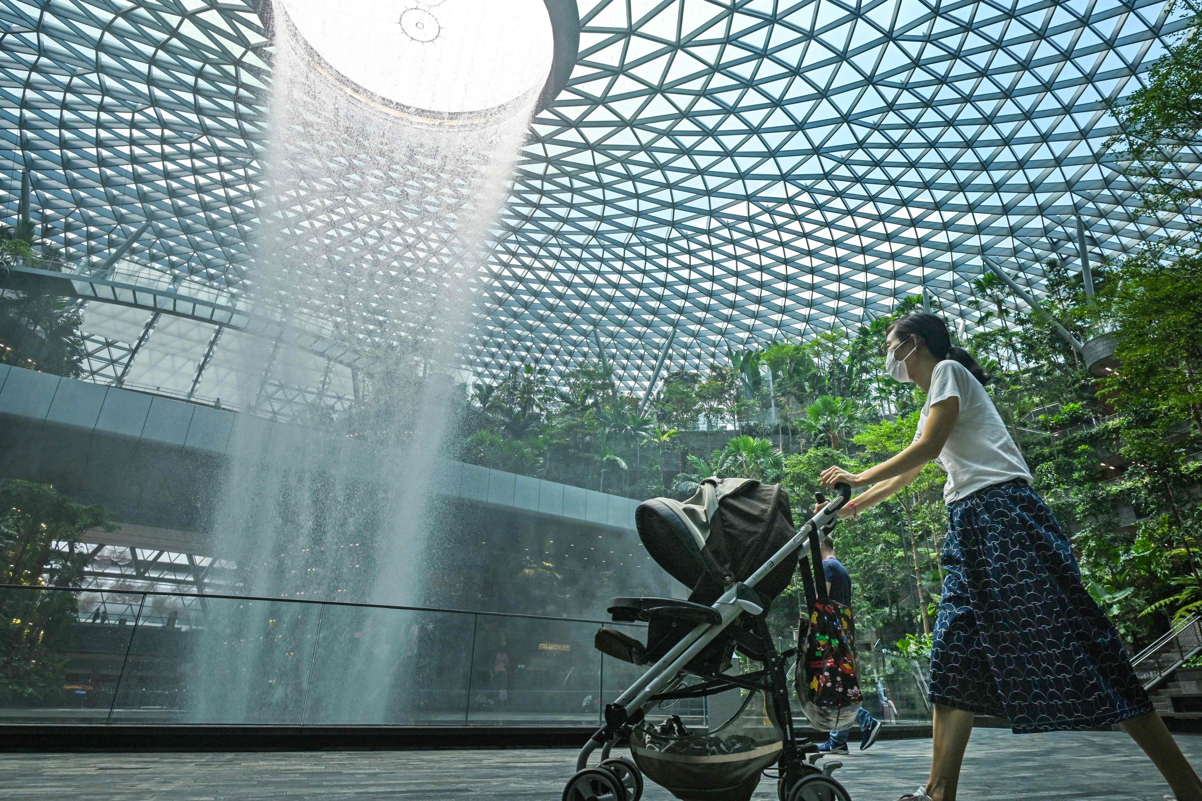 A woman pushes a baby stroller past the rain vortex at Jewel Changi Airport in Singapore. Photo: AFP