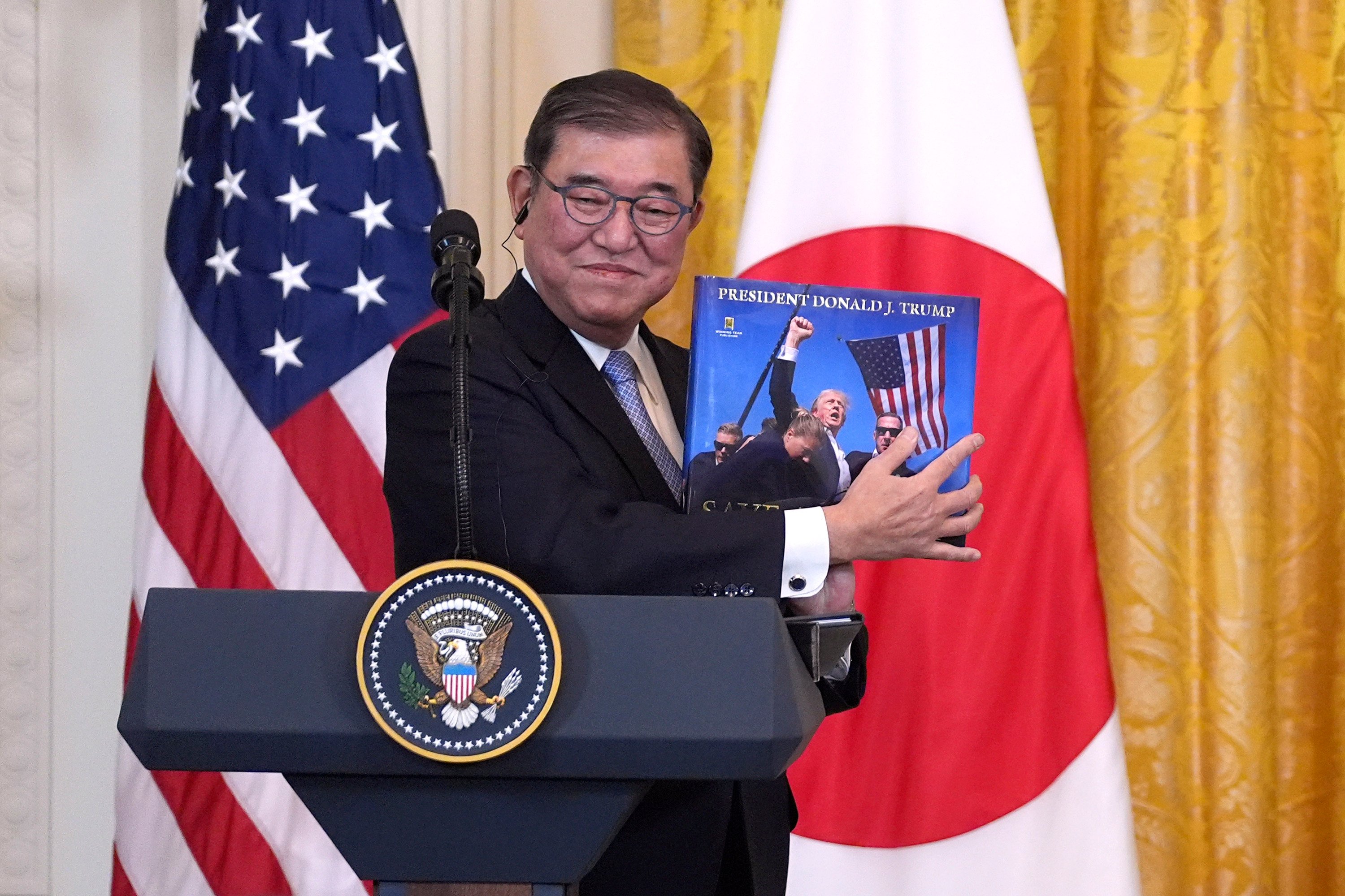 Japanese Prime Minister Shigeru Ishiba holds a book presented to him by US President Donald Trump during a news conference in Washington on Friday. Photo: AP