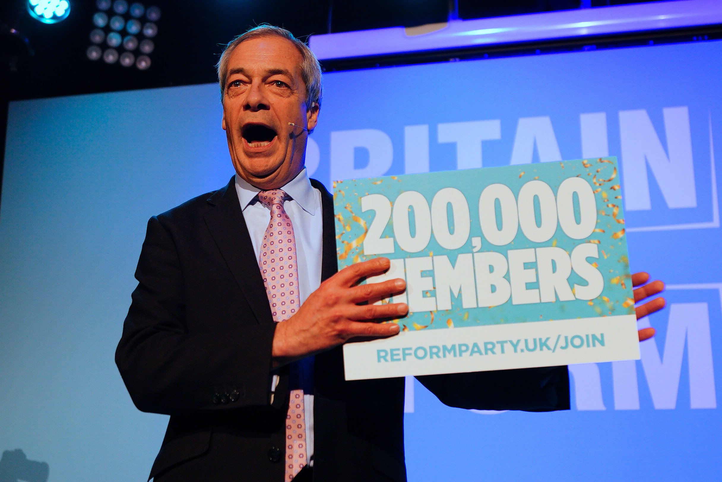 Reform UK leader Nigel Farage holds a sign announcing that the party has more than 200,000 members, during the Reform UK Wiltshire conference at the Civic Trowbridge, Wiltshire, England. Photo: PA Wire / dpa