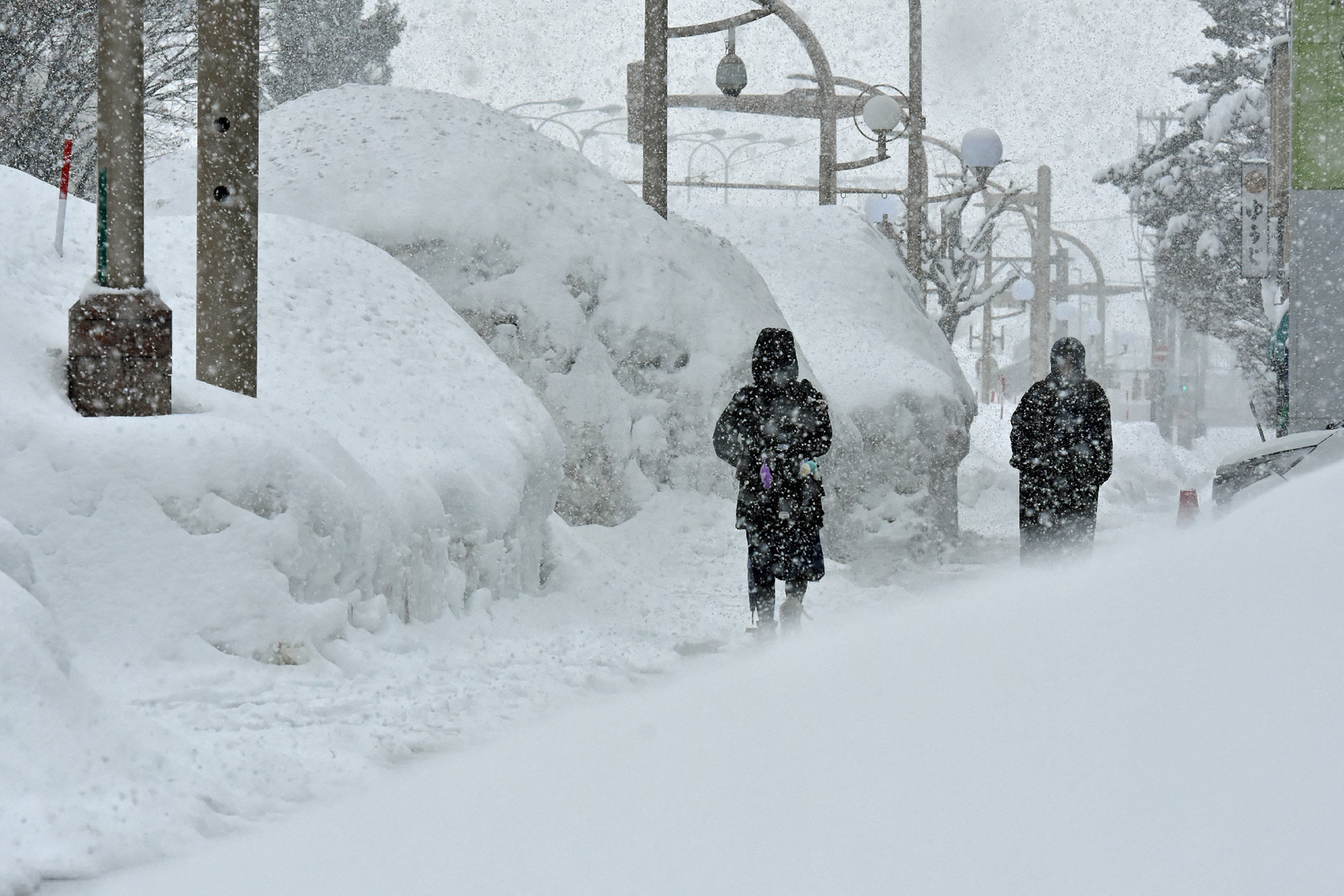 Pedestrians walk past high drifts of snow along a street in the northern Japanese city of Aomori on January 9, 2025. The area’s apple trees have been damaged by the weight of the snow. Photo: AFP