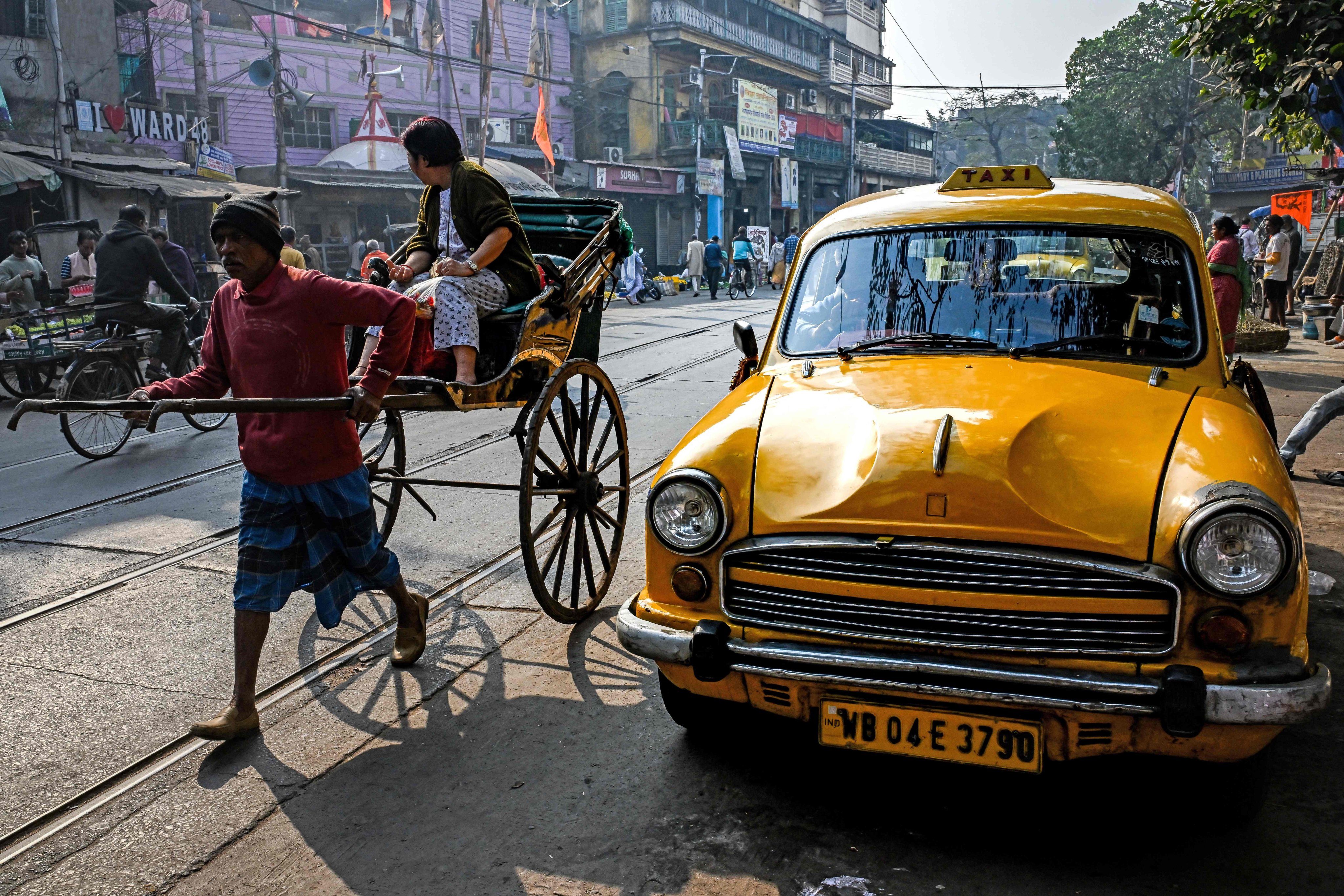 A woman rides a rickshaw past a Hindustan Ambassador yellow taxi, parked on a roadside in Kolkata. The one-time Indian capital is mourning the slow death of its stately yellow cabs. Photo: AFP