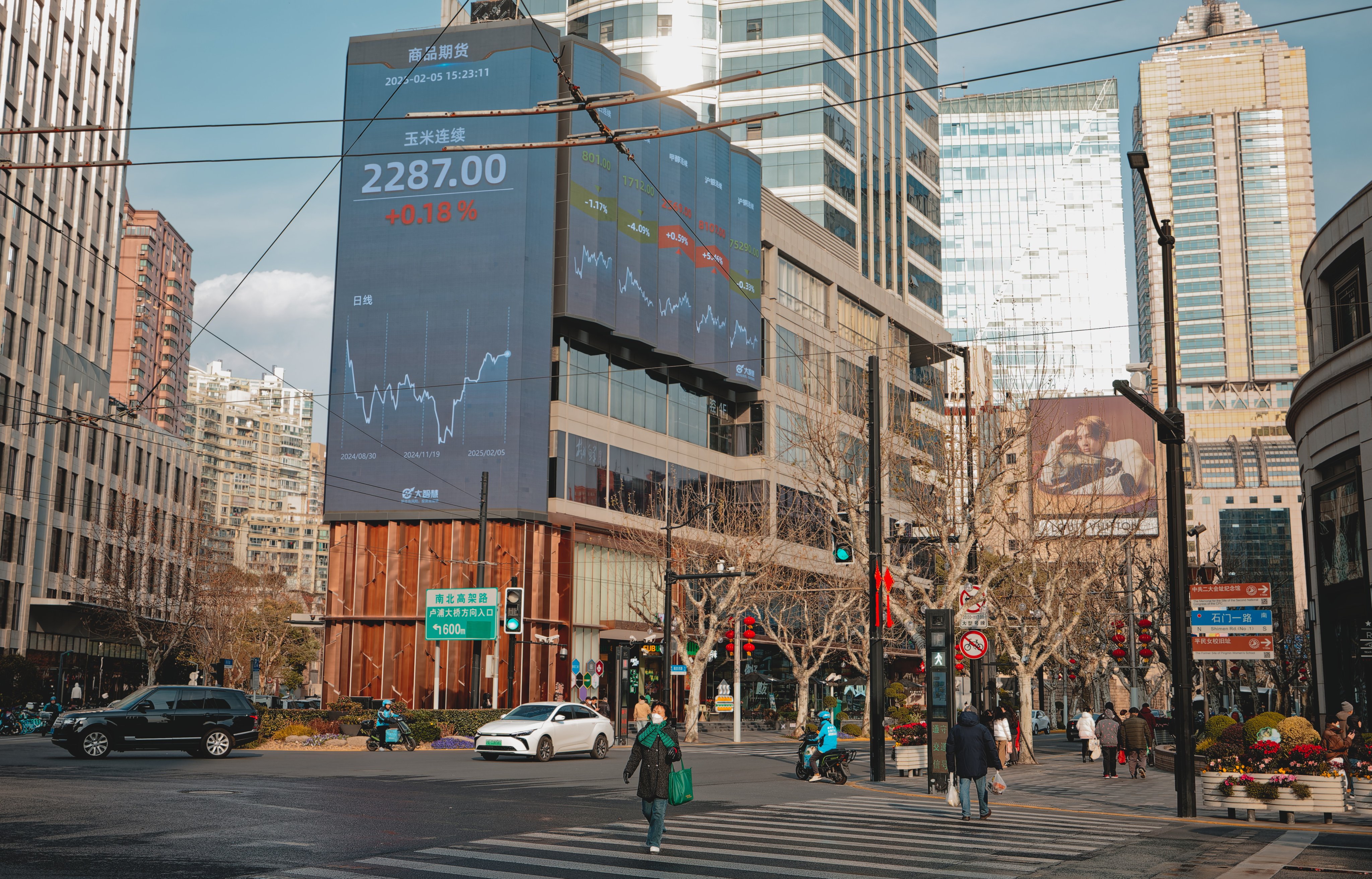 People cross a street near a screen showing stock exchange and economic data in Shanghai. Photo: EPA-EFE