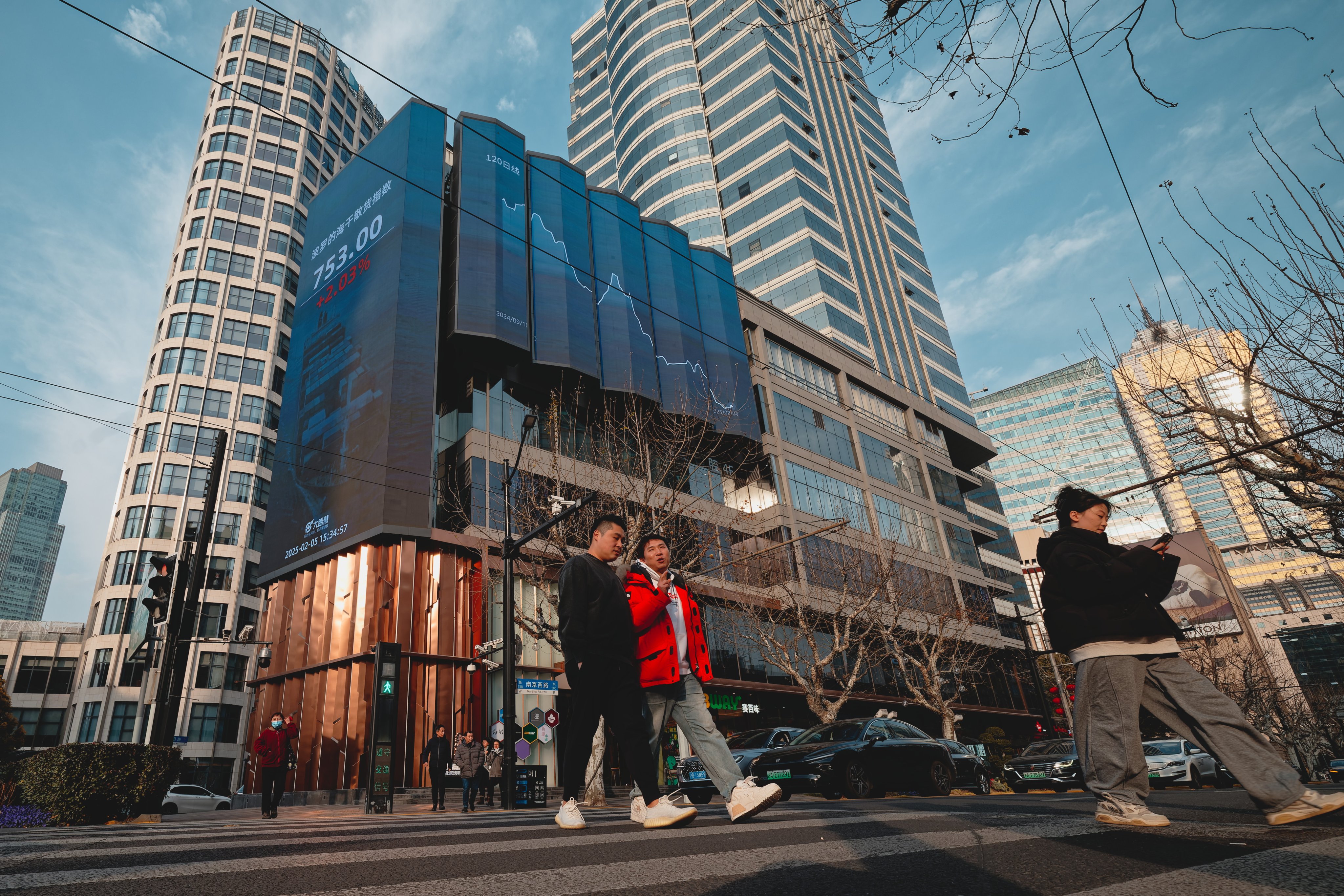 People cross a street near a screen showing stock exchange and economic data in Shanghai on February 5, 2025. Photo: EPA-EFE