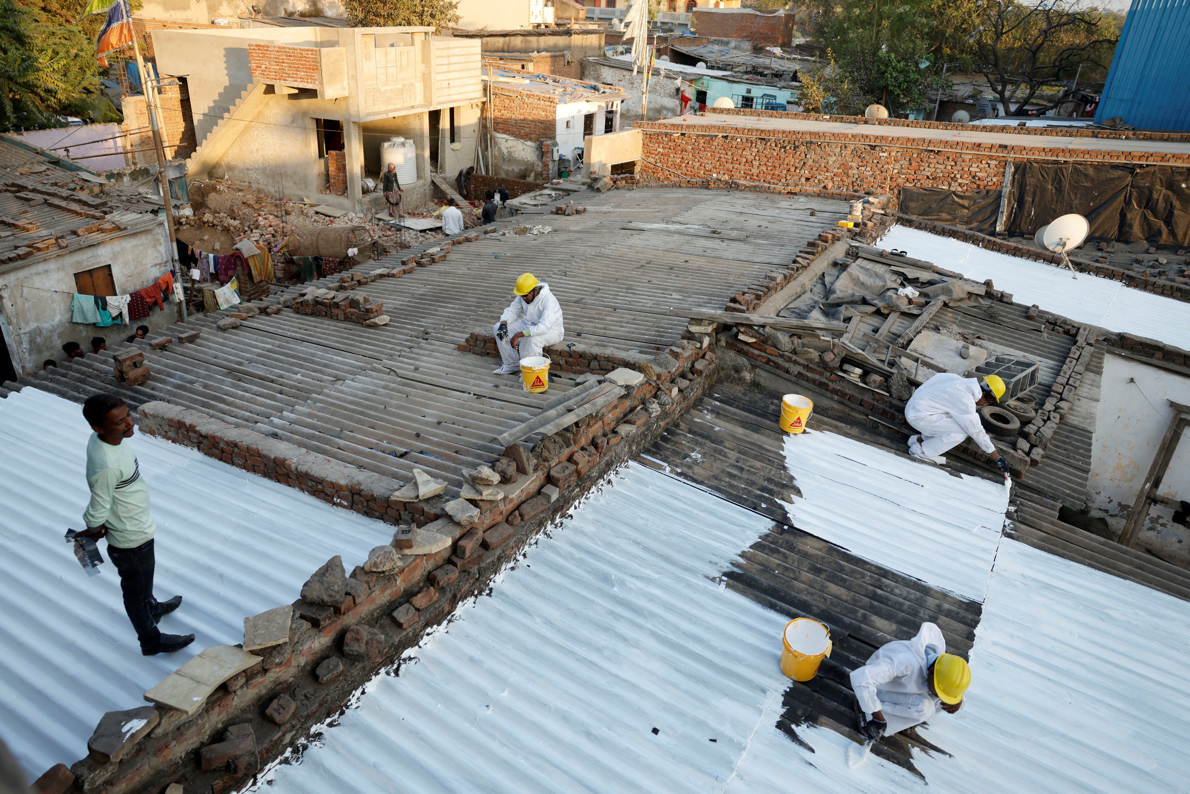 Workers paint on a liquid-applied membrane to shanties at a slum in Ahmedabad, India. Photo: Reuters