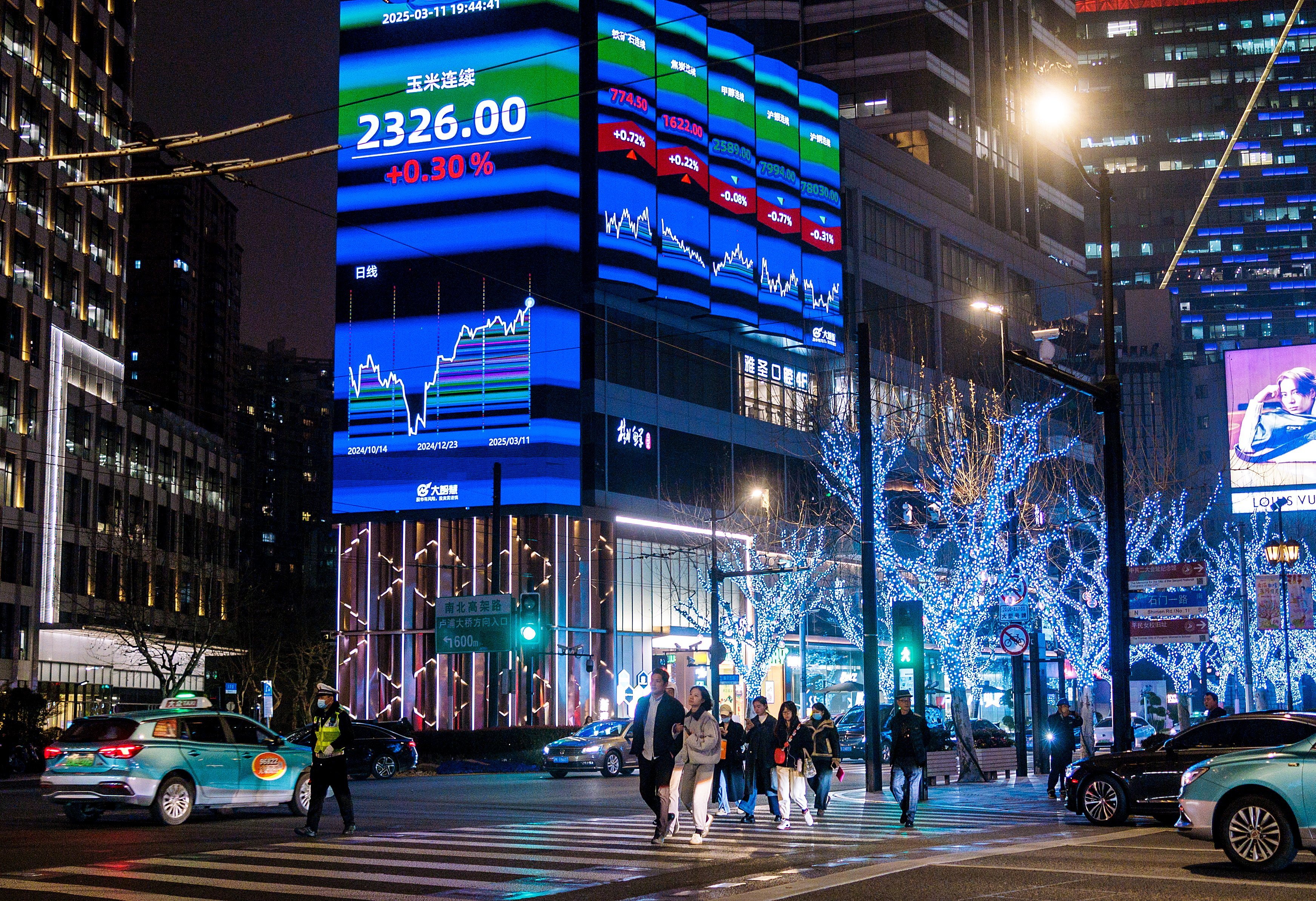 People cross a street in front of a large screen displaying the latest stock market and economy data, in Shanghai on March 11. Photo: EPA-EFE