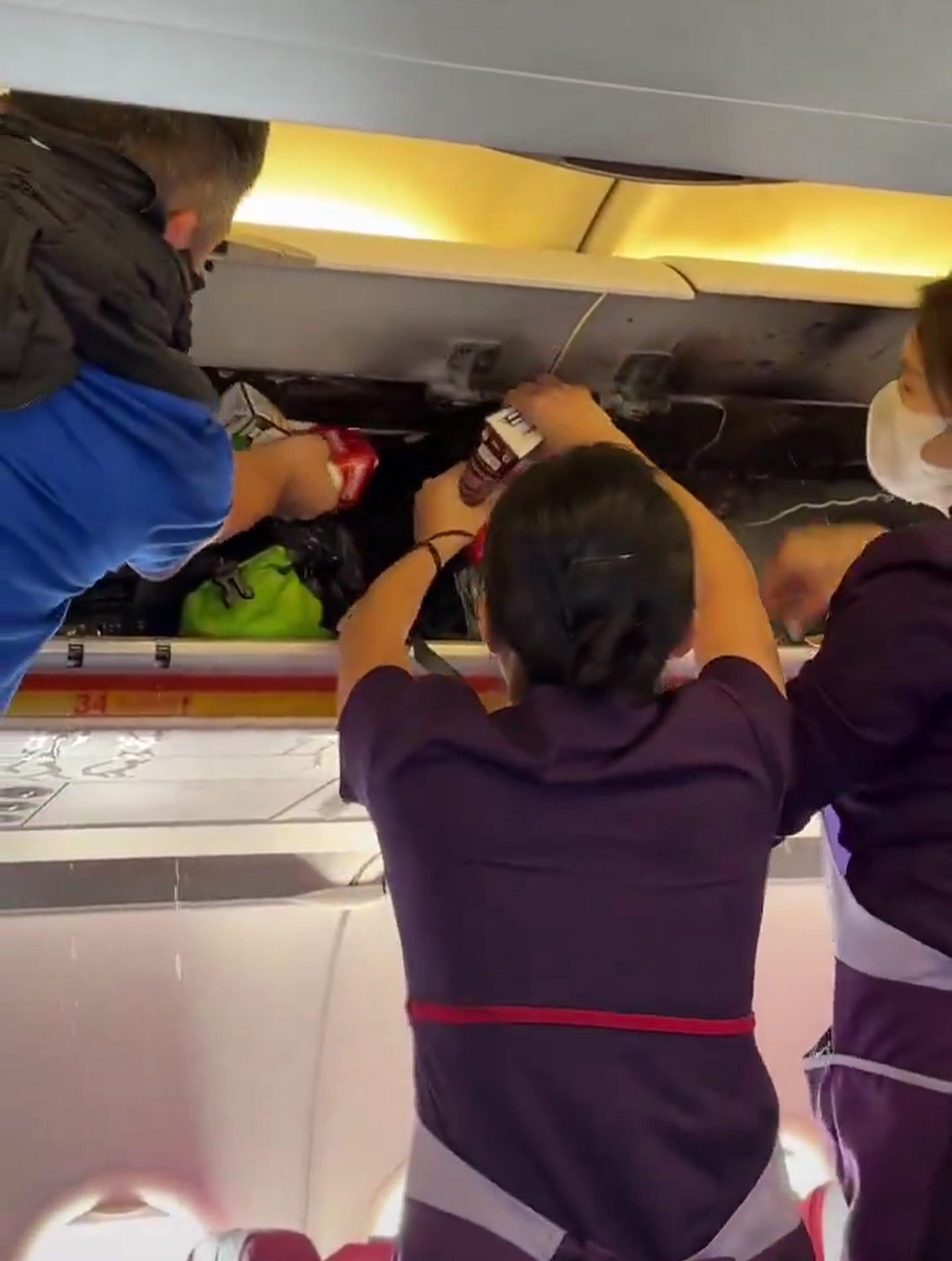 A screengrab shows cabin crew members and passengers using drinks to put out the fire in the overhead locker. Photo: SCMP