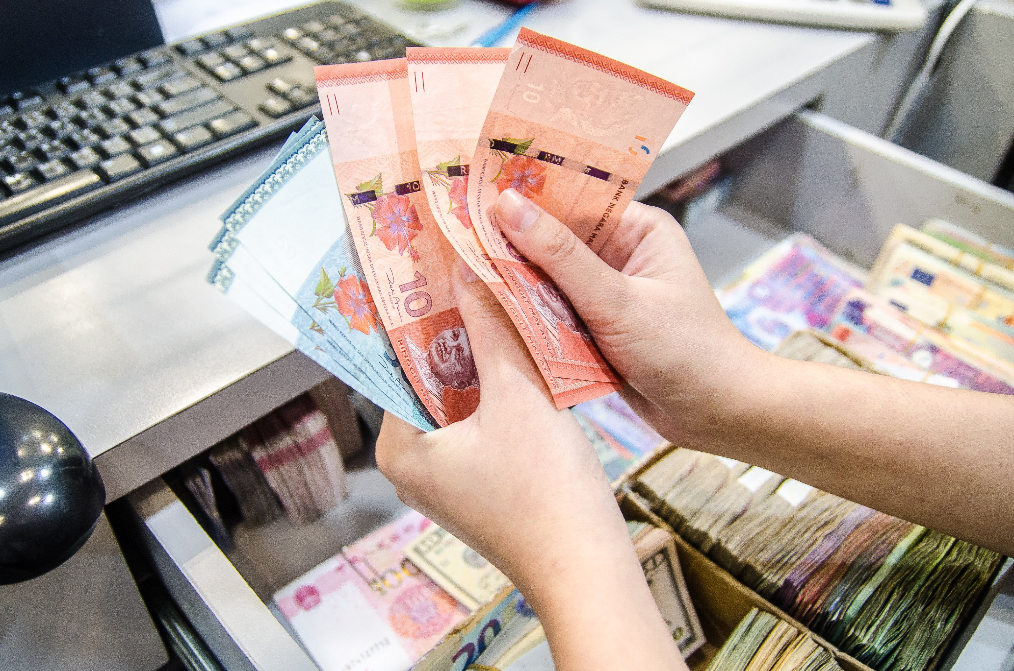 Women counts Malaysian ringgit. Malaysia has postponed a sales tax expansion to ease business strain from US tariffs. Photo: Shutterstock