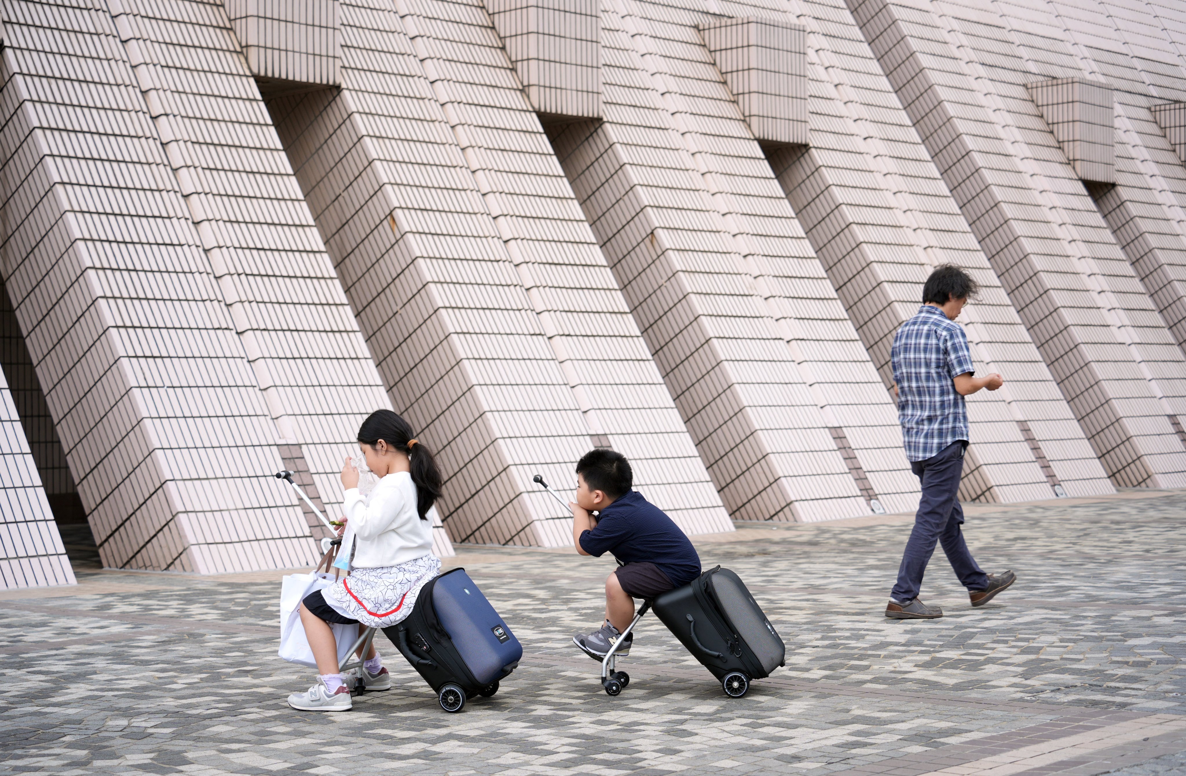 Two young tourists sit on their ride-on suitcases outside Hong Kong Cultural Centre in Tsim Sha Tsui. Photo: Eugene Lee