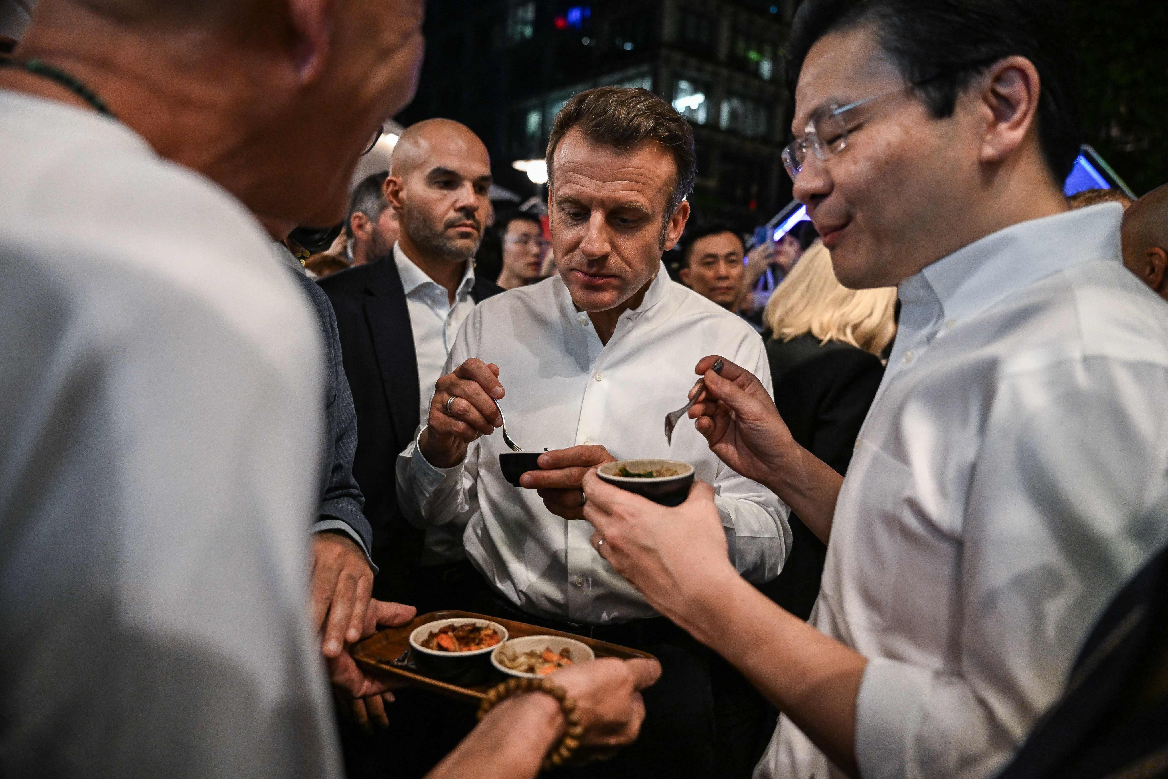 French President Emmanuel Macron (centre) and Singapore’s Prime Minister Lawrence Wong (right) try snacks during their visit to the Lau Pau Sat hawker centre on May 29. Photo: AFP