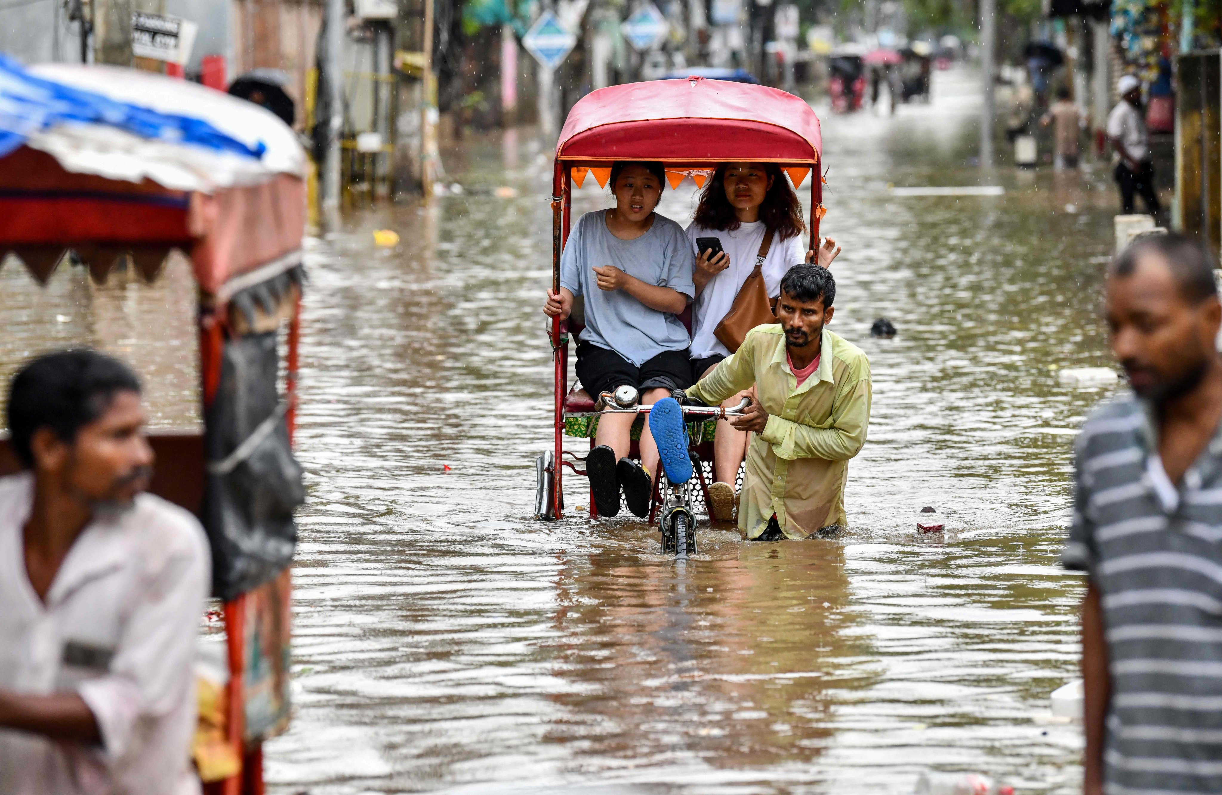 Women commute in cycle rickshaws through a flooded street after heavy rains in Guwahati, in India’s Assam state, on Saturday. Photo: AFP