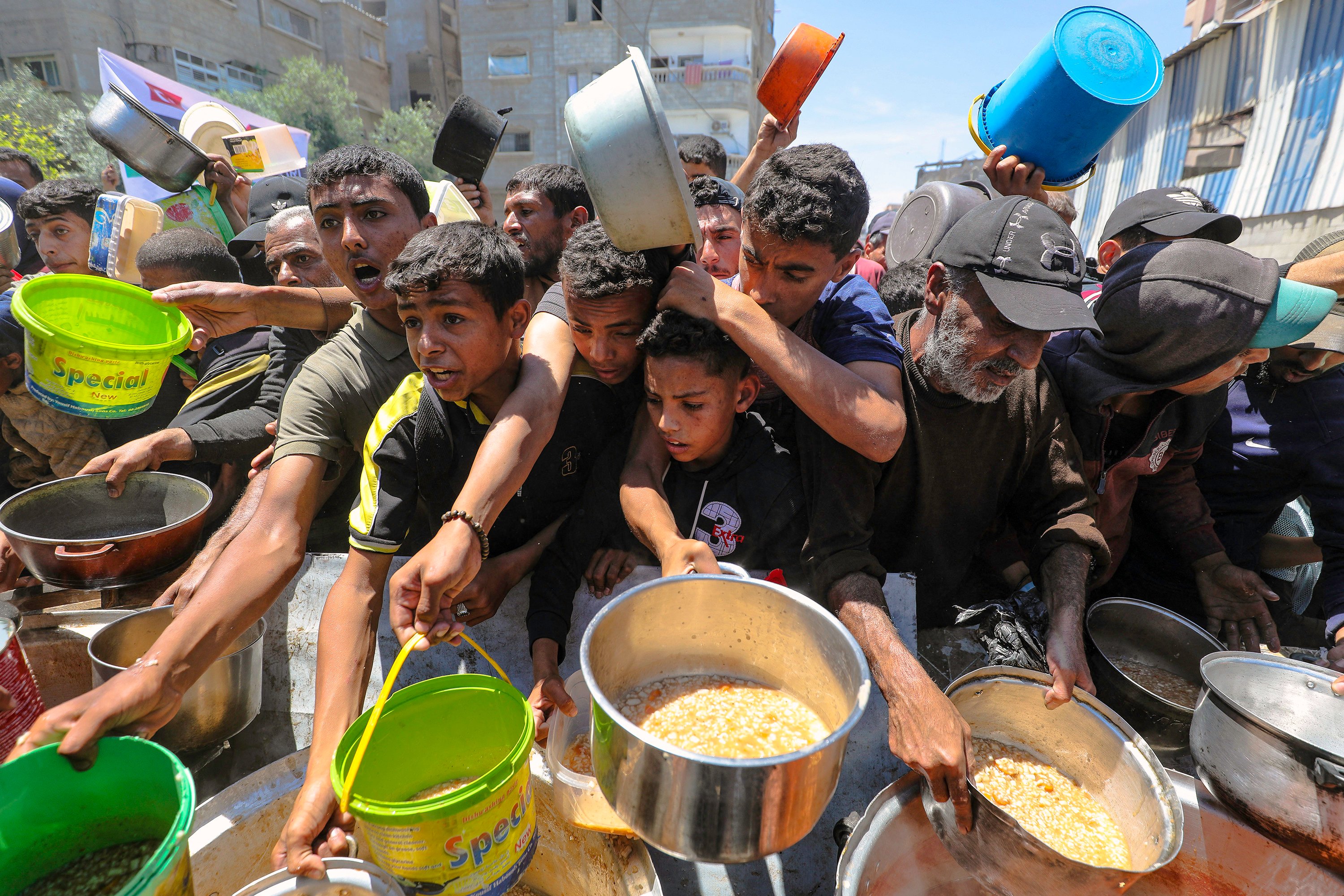 Hungry displaced Palestinians rush to food distribution kitchen and extend their empty containers to receive food in Gaza. Photo: TNS