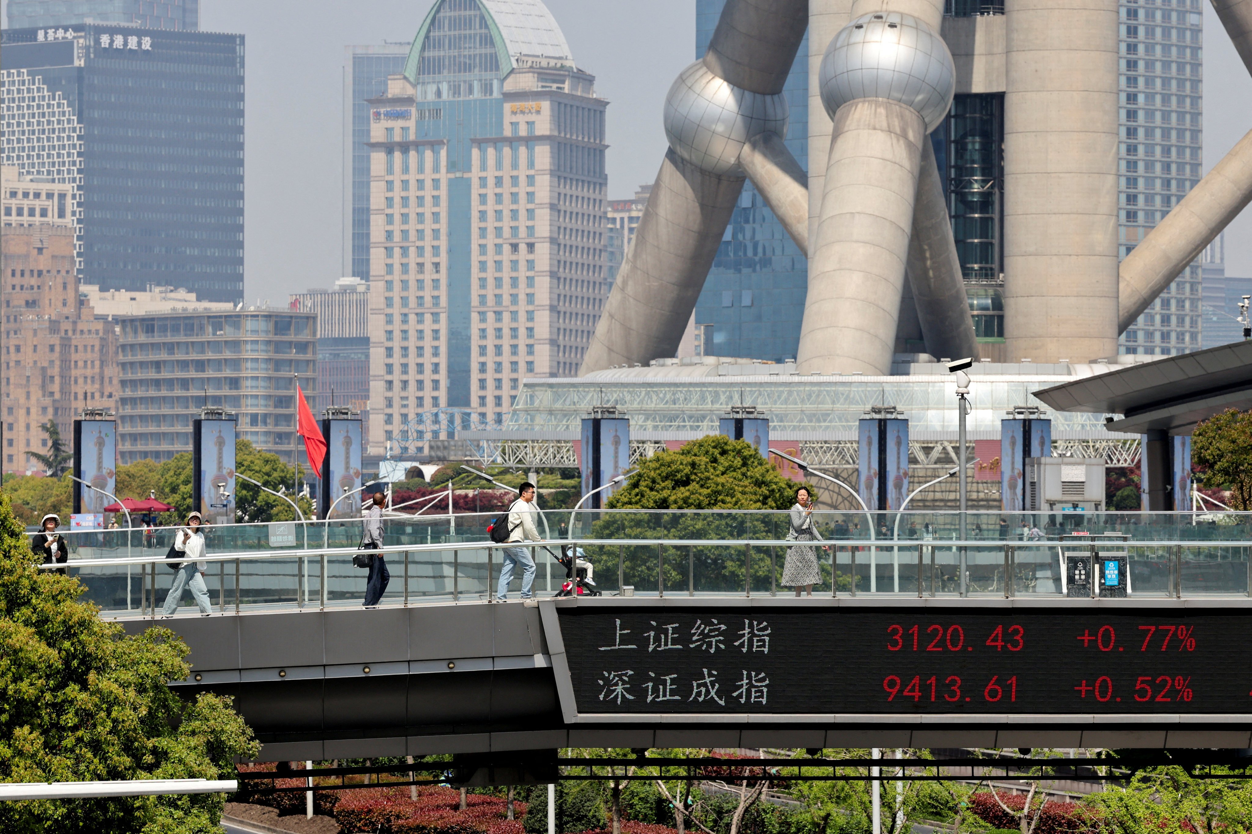 An electronic board shows Shanghai and Shenzhen stock indices as people walk on a pedestrian bridge at the Lujiazui financial district in Shanghai on April 8, 2025. Photo: Reuters