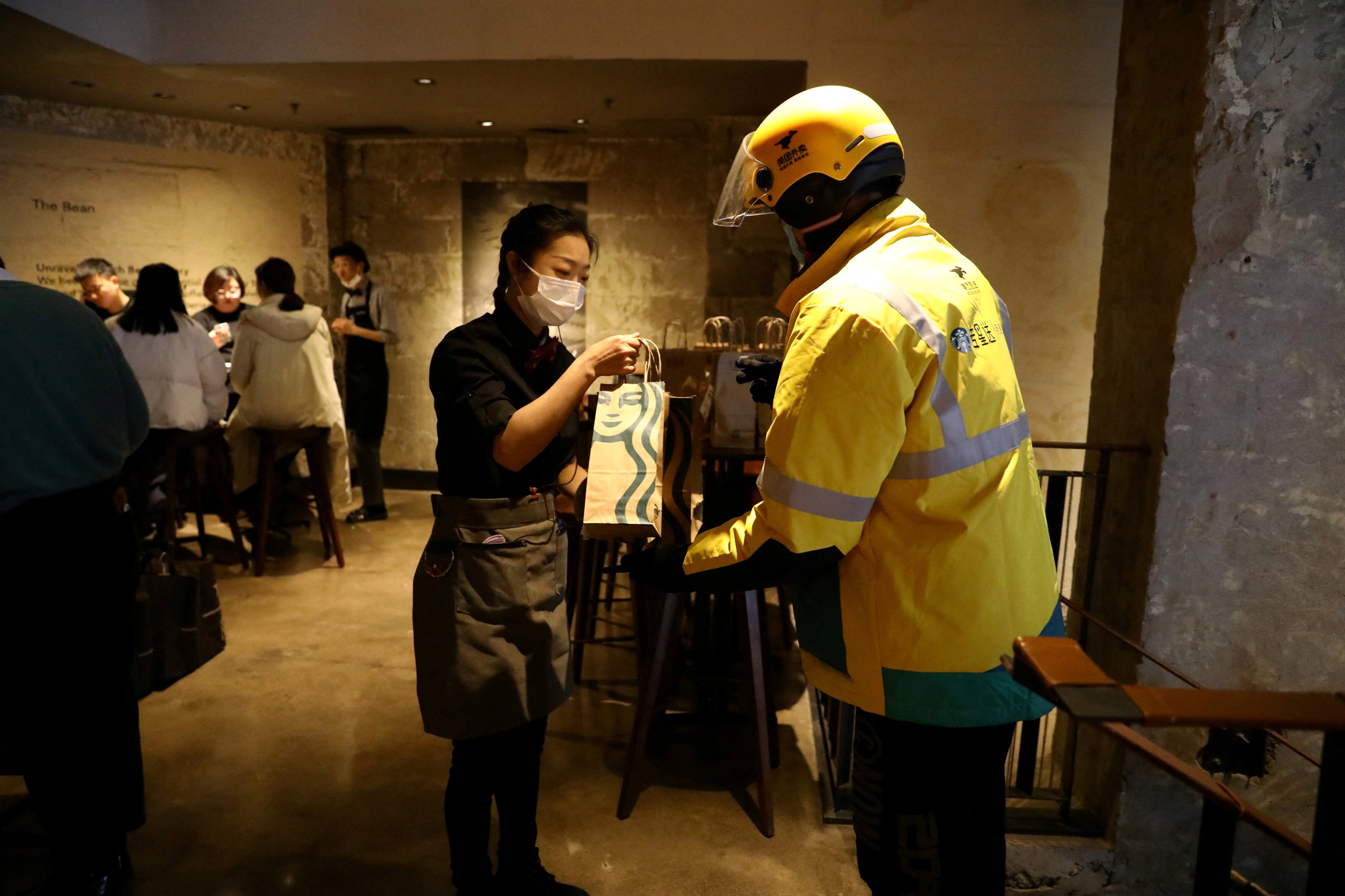 A staff member takes a bag of ordered food from a Meituan delivery worker during a Starbucks media event in Beijing on January 18, 2022. Photo: Reuters