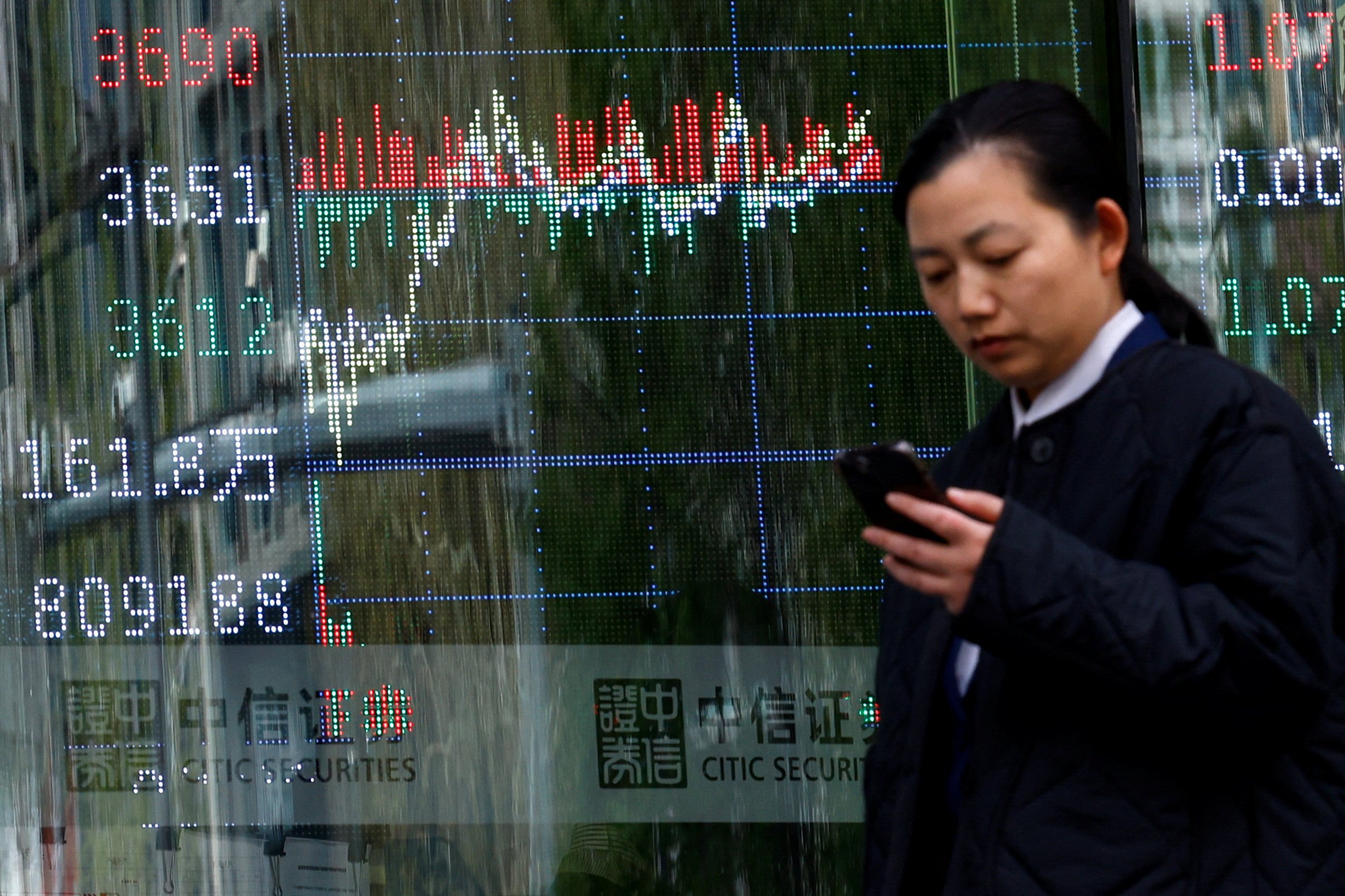 A woman walks past a brokerage house with a display board showing the stock index information in Beijing. Photo: Reuters