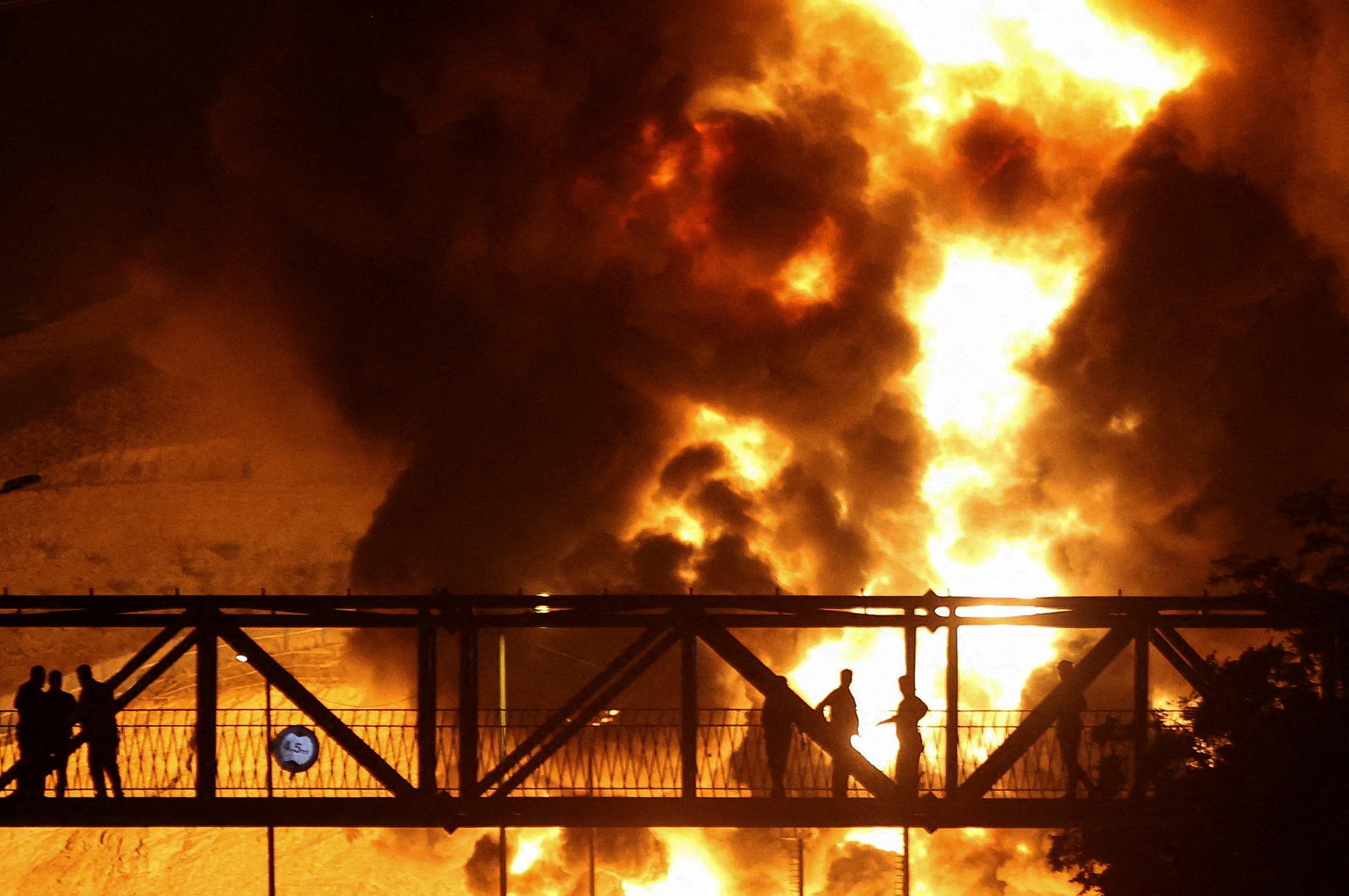 People watch from a bridge as flames from an Israeli attack rise from the Sharan Oil depot in Tehran, Iran, on June 15. Photo: Reuters