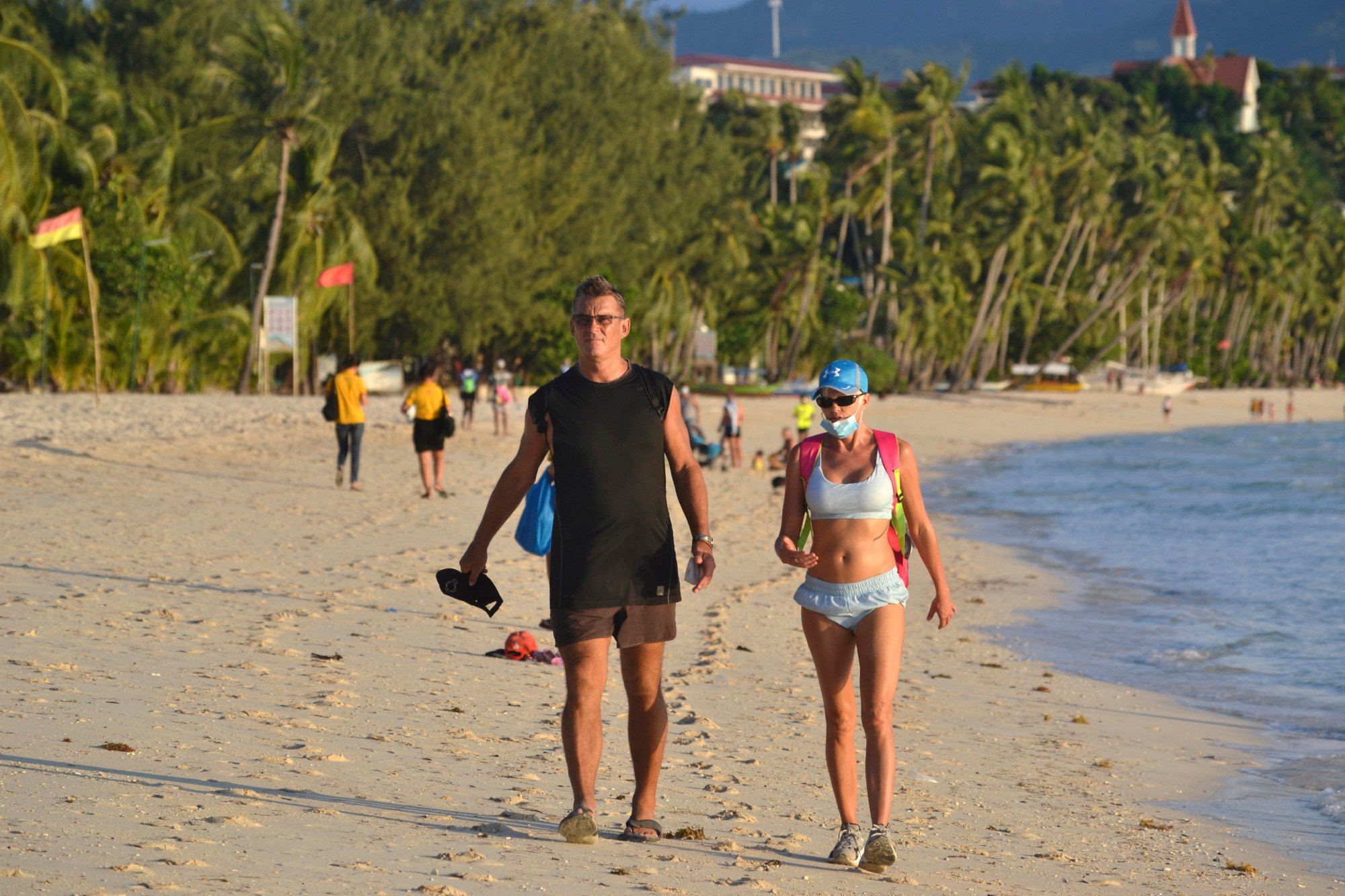 Tourists walk along the shores of Boracay beach. The island was closed temporarily in 2018 due to overtourism. Photo: AP Tourists walk along the shores of Boracay beach. The island was closed temporarily in 2018 due to overtourism. Photo: AP