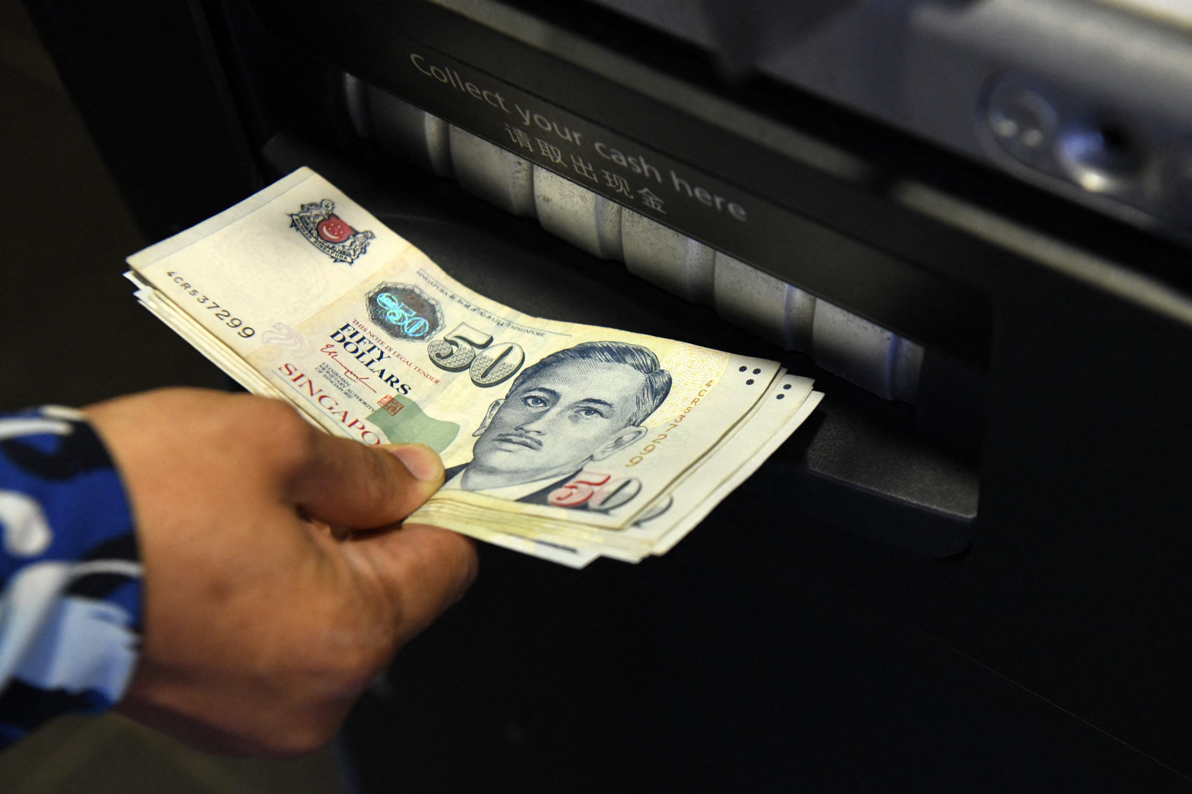 A man withdraws Singapore dollar banknotes from an ATM. Scam victims will still be allowed to withdraw funds for daily living expenses. Photo: AFP