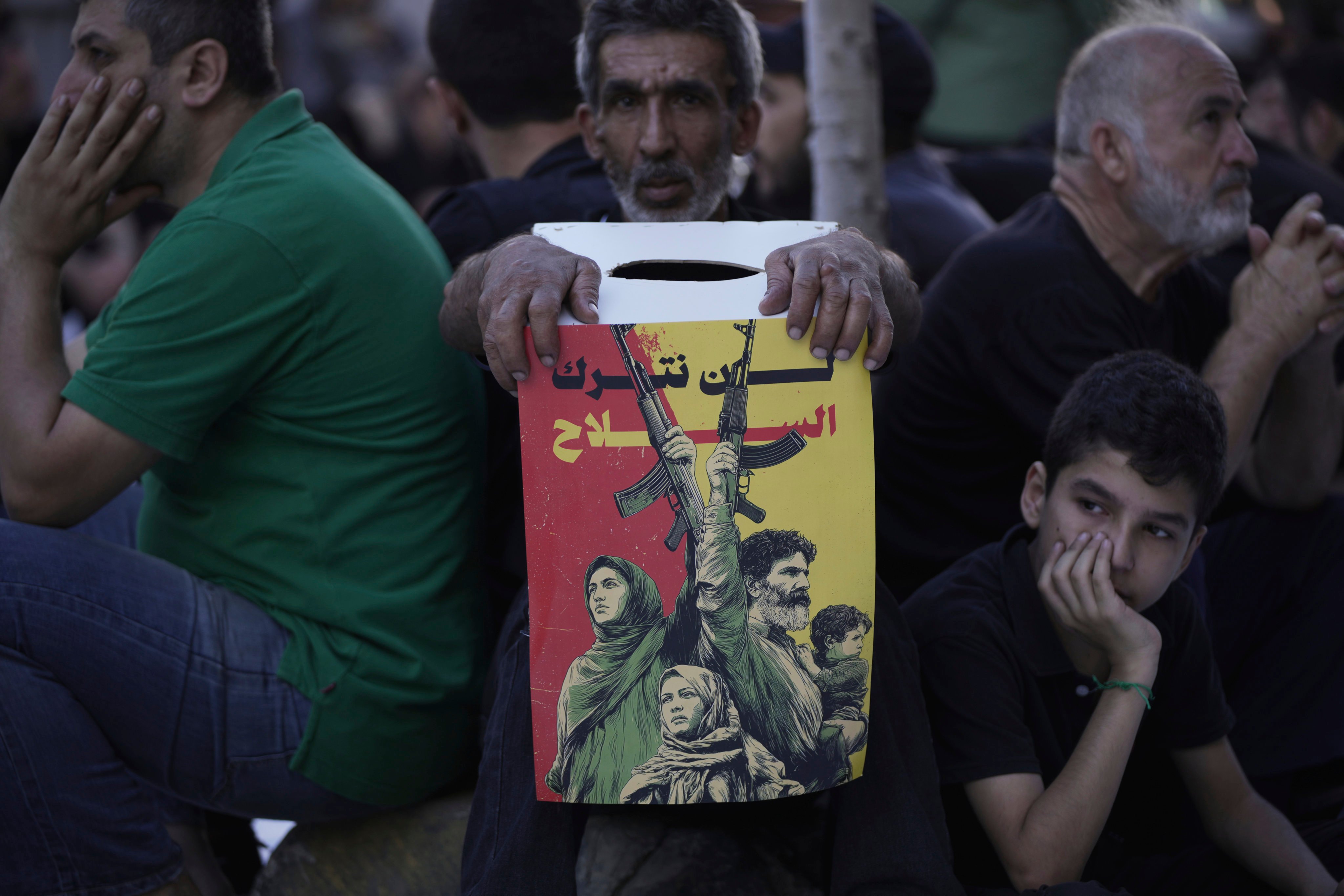 A Hezbollah supporter holds a poster reading ‘We shall not abandon our weapons’ as others listen during a Shiite sermon, in Beirut, Lebanon, on Sunday. Photo: AP