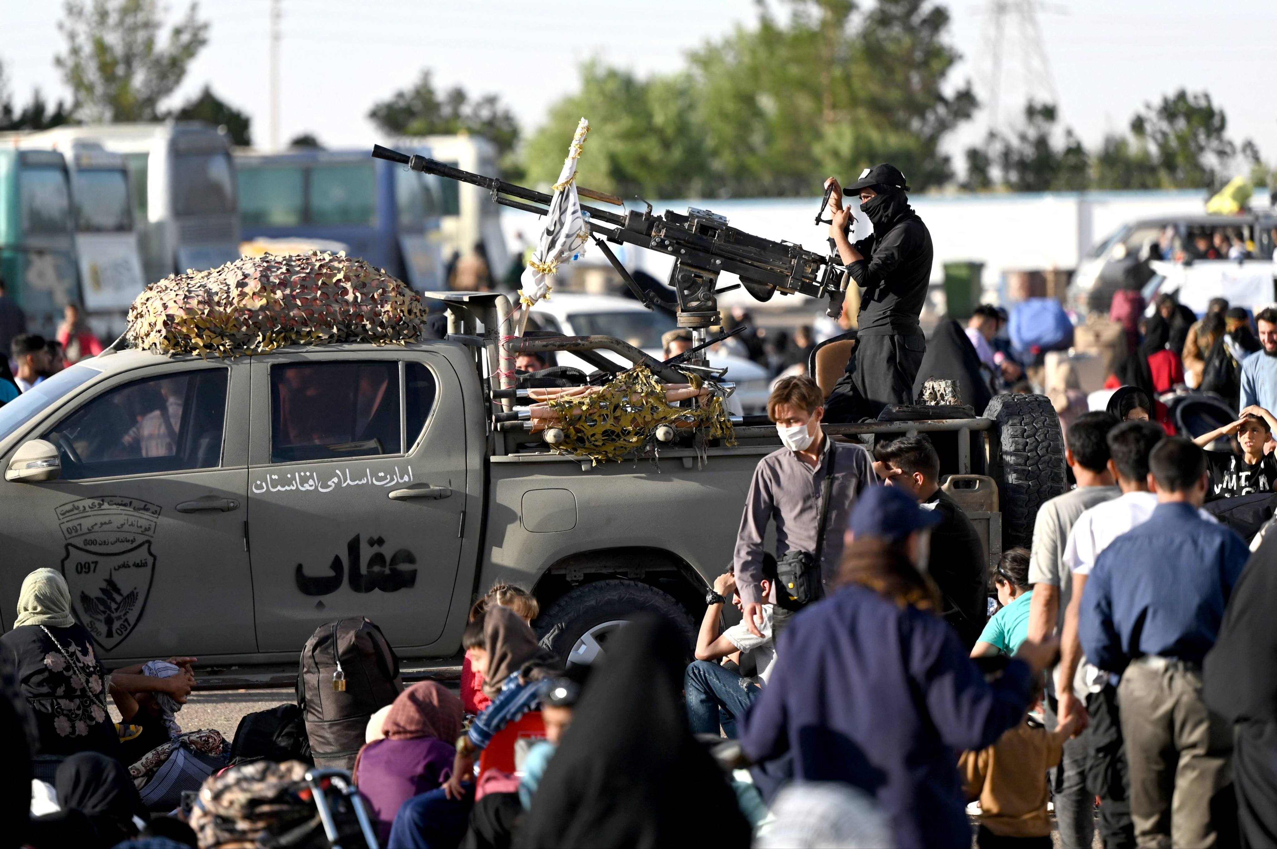 Taliban security personnel stand guard on the back of a vehicle as Afghan refugees arrive at the zero point of the Islam Qala border crossing between Afghanistan and Iran on June 28, following their deportation from Iran. Photo: AFP