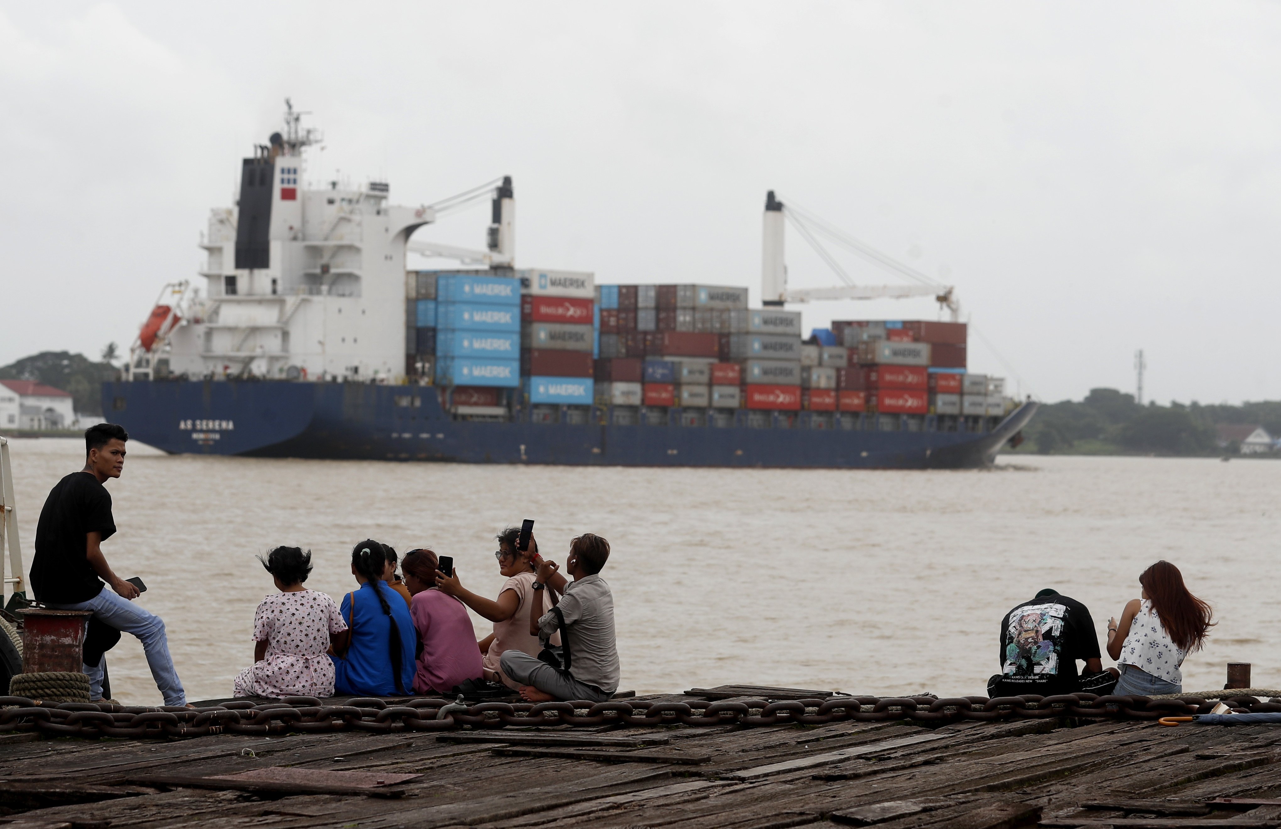 People relax at the jetty near the container cargo port on Wednesday as a container cargo ship passes by in Myanmar, which US President Donald Trump has threatened with a 40 per cent tariff. Photo: EPA