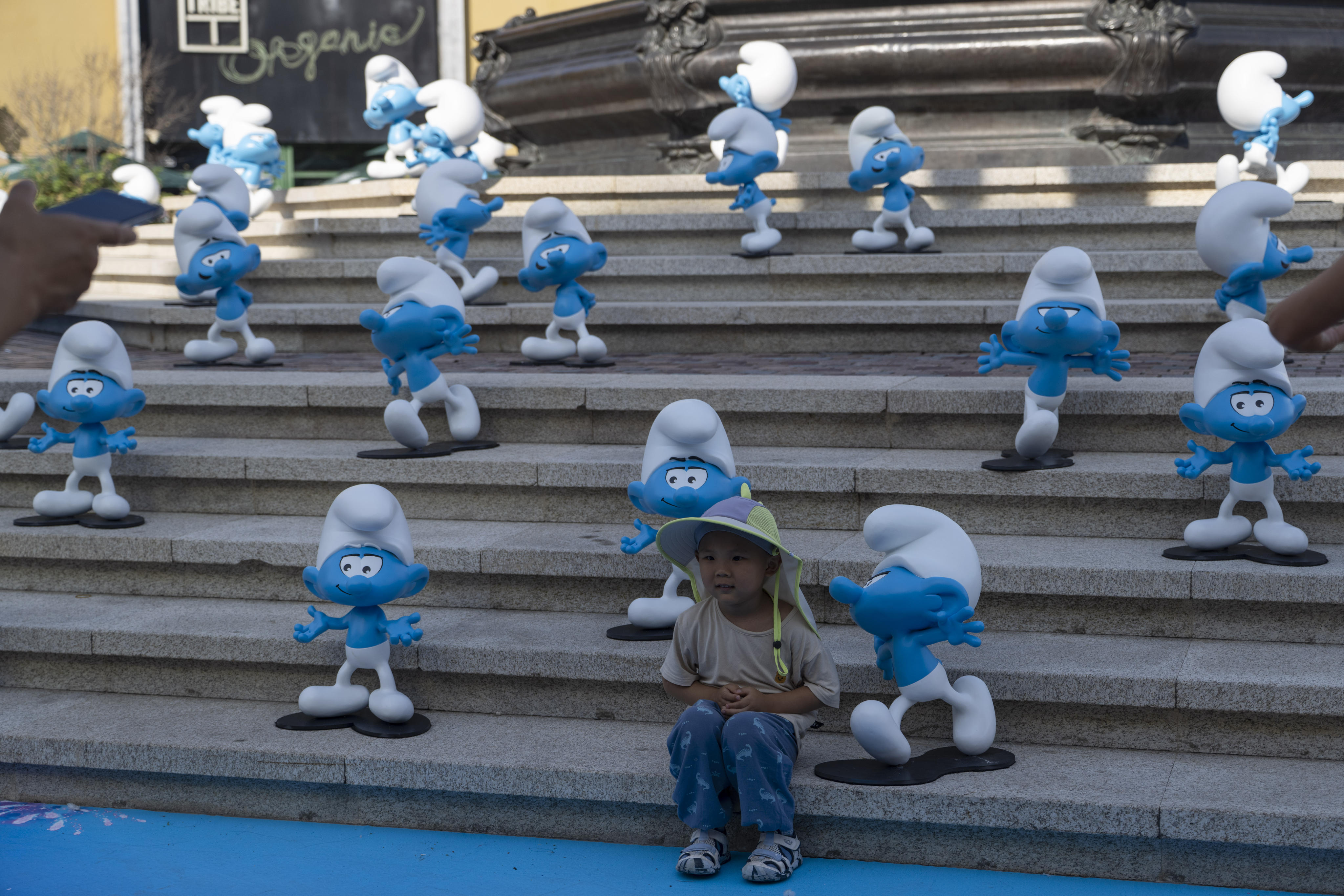 A child sits with life-size blue figures – characters from the upcoming ‘Smurf’ film – in Beijing, China. Photo: AP