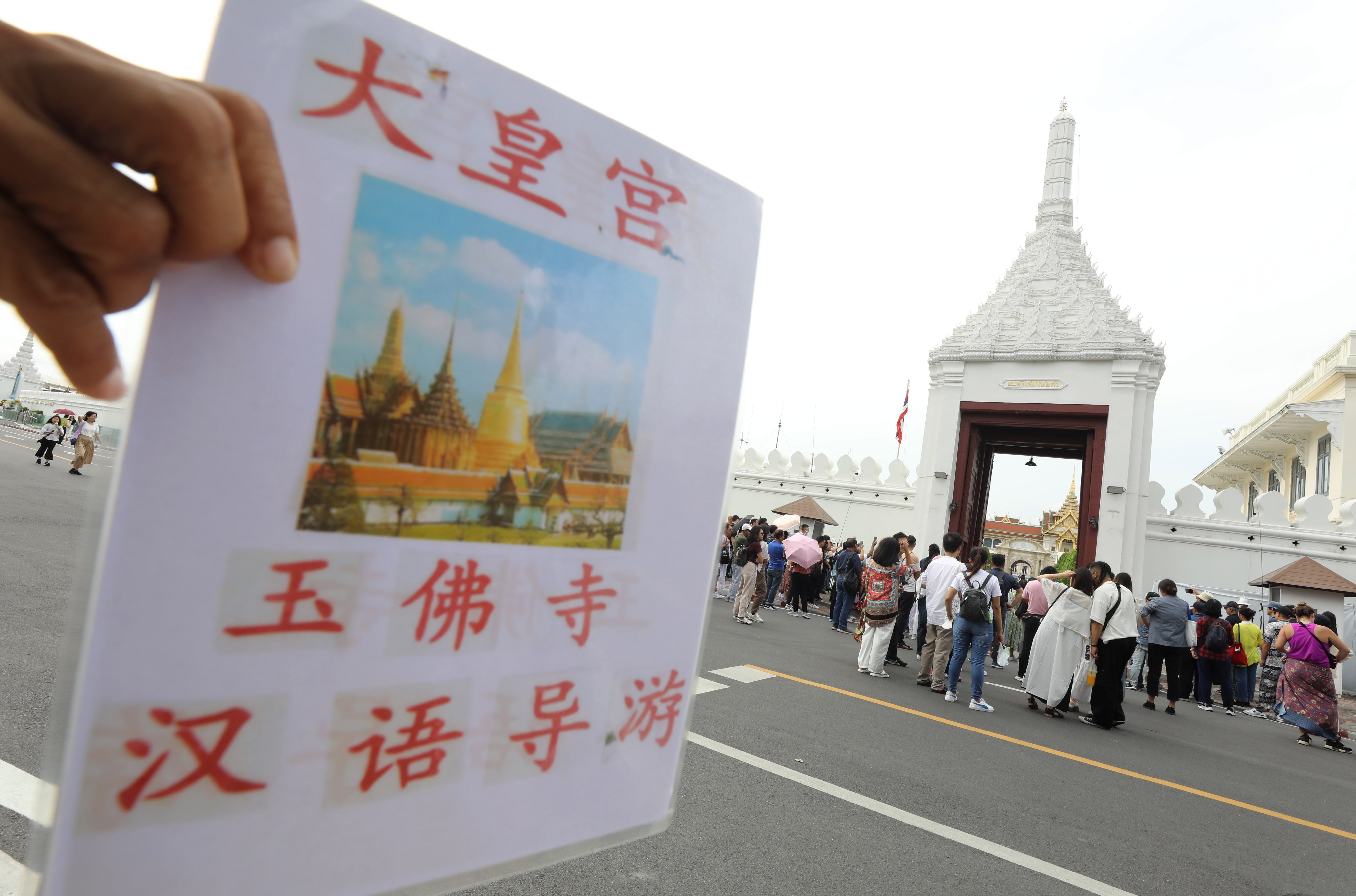 Chinese tourists and others wait to visit the Emerald Buddha Temple inside of the Grand Palace, next to a tour guide sign written in Chinese characters. Photo: EPA-EFE